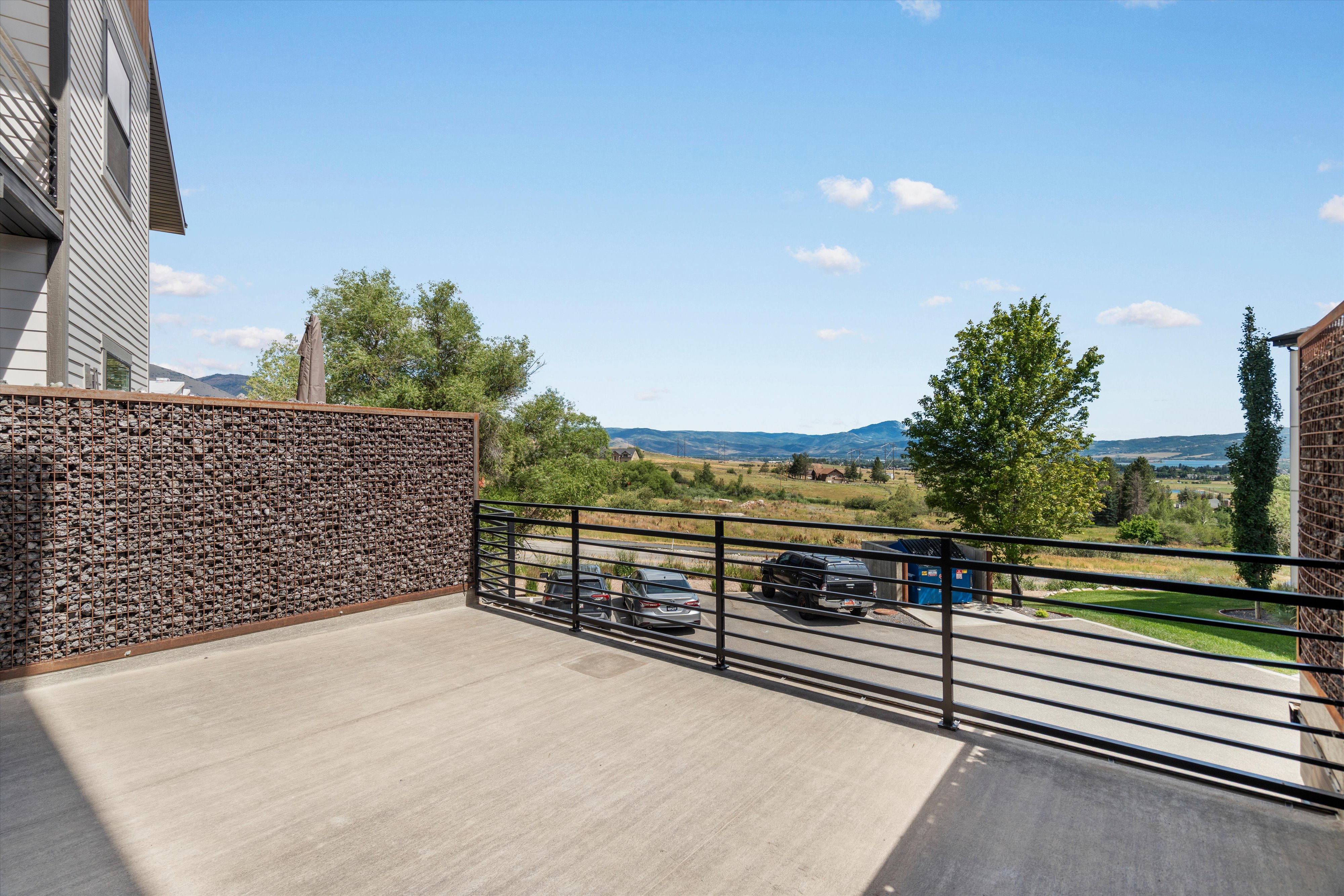 Spacious outdoor balcony featuring a concrete surface, contemporary horizontal metal railing, and a decorative gabion wall