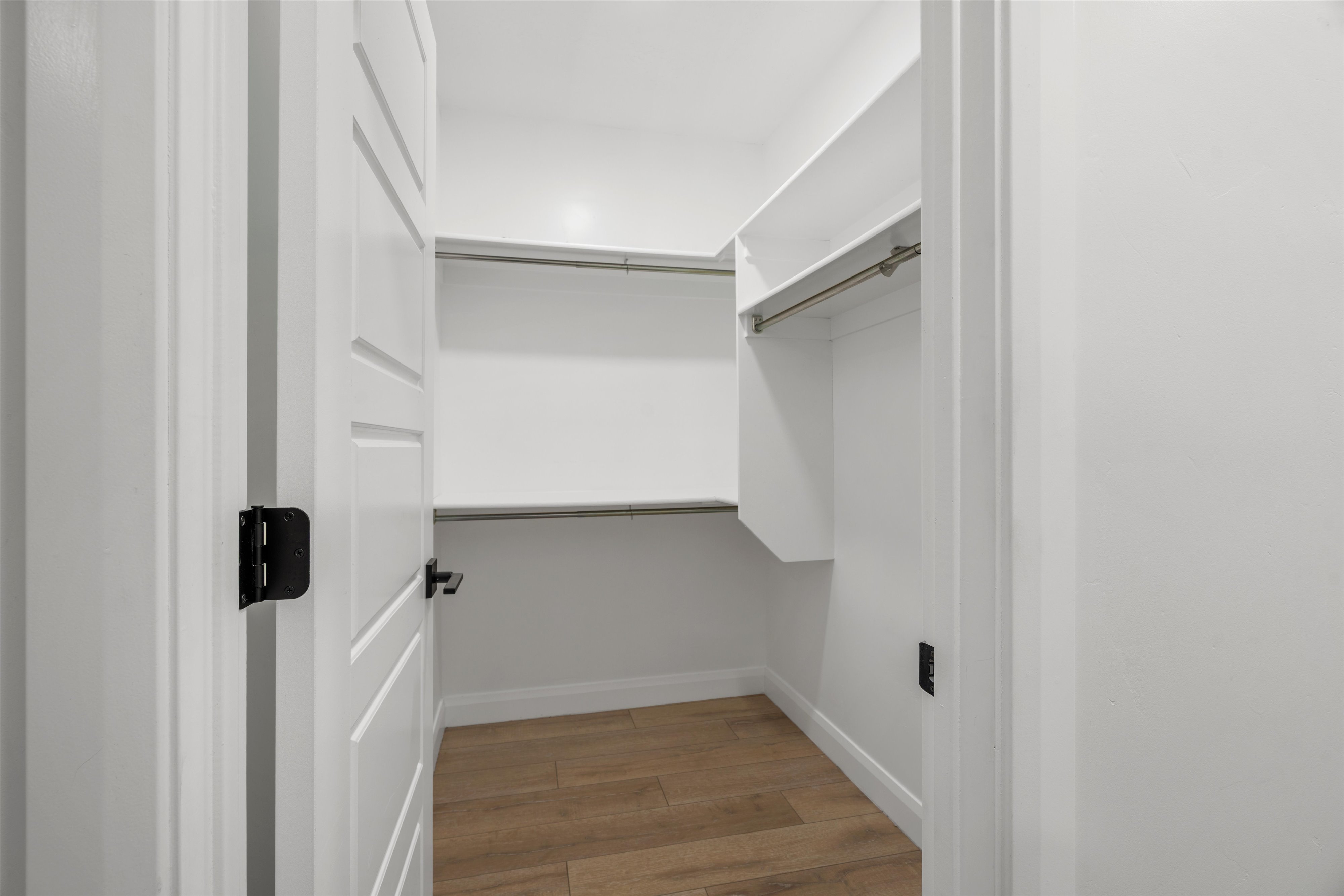 Walk-in closet featuring built-in shelving, hanging rods, and wood-finish flooring