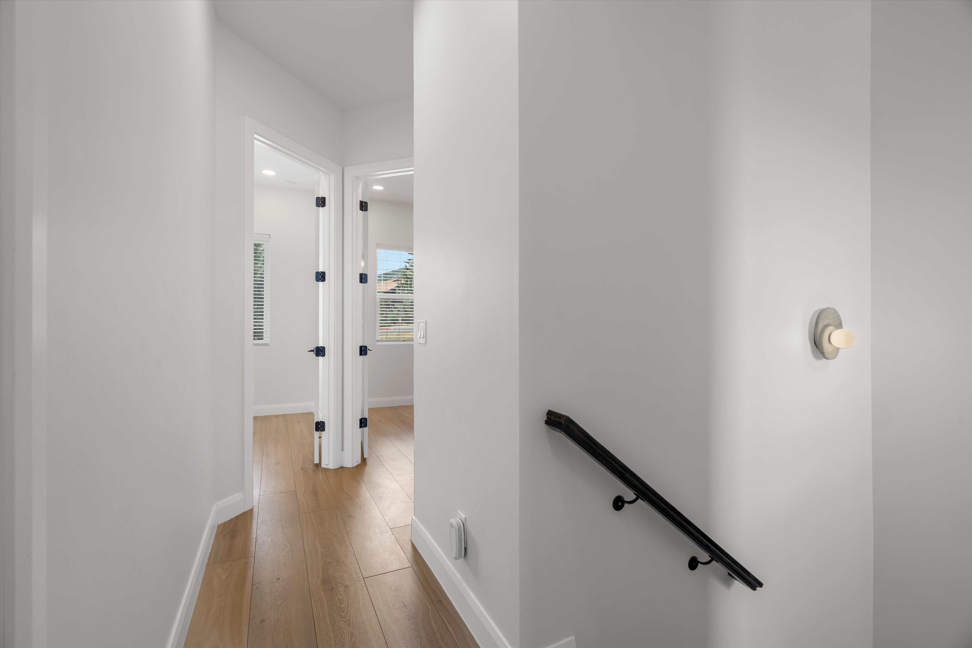 Hallway featuring light wood-finish flooring, white baseboards, and a contemporary wall sconce