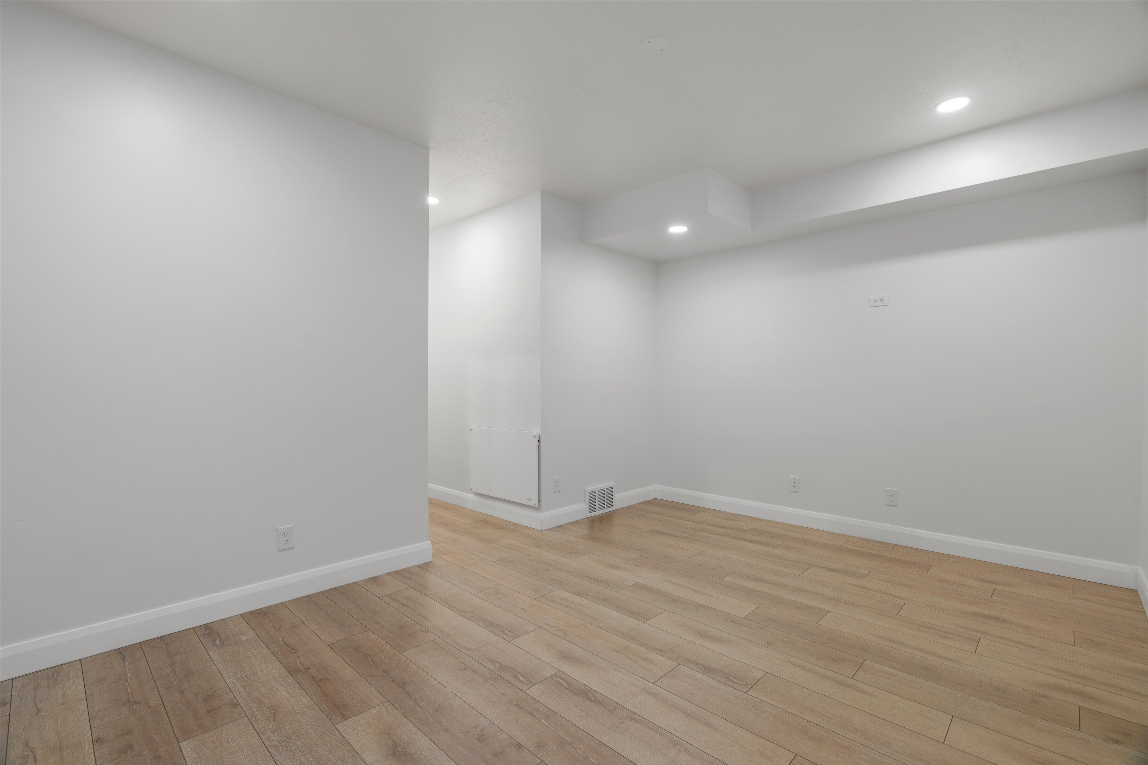 Spacious interior room featuring light wood-finish flooring, white baseboards, and neutral wall tones