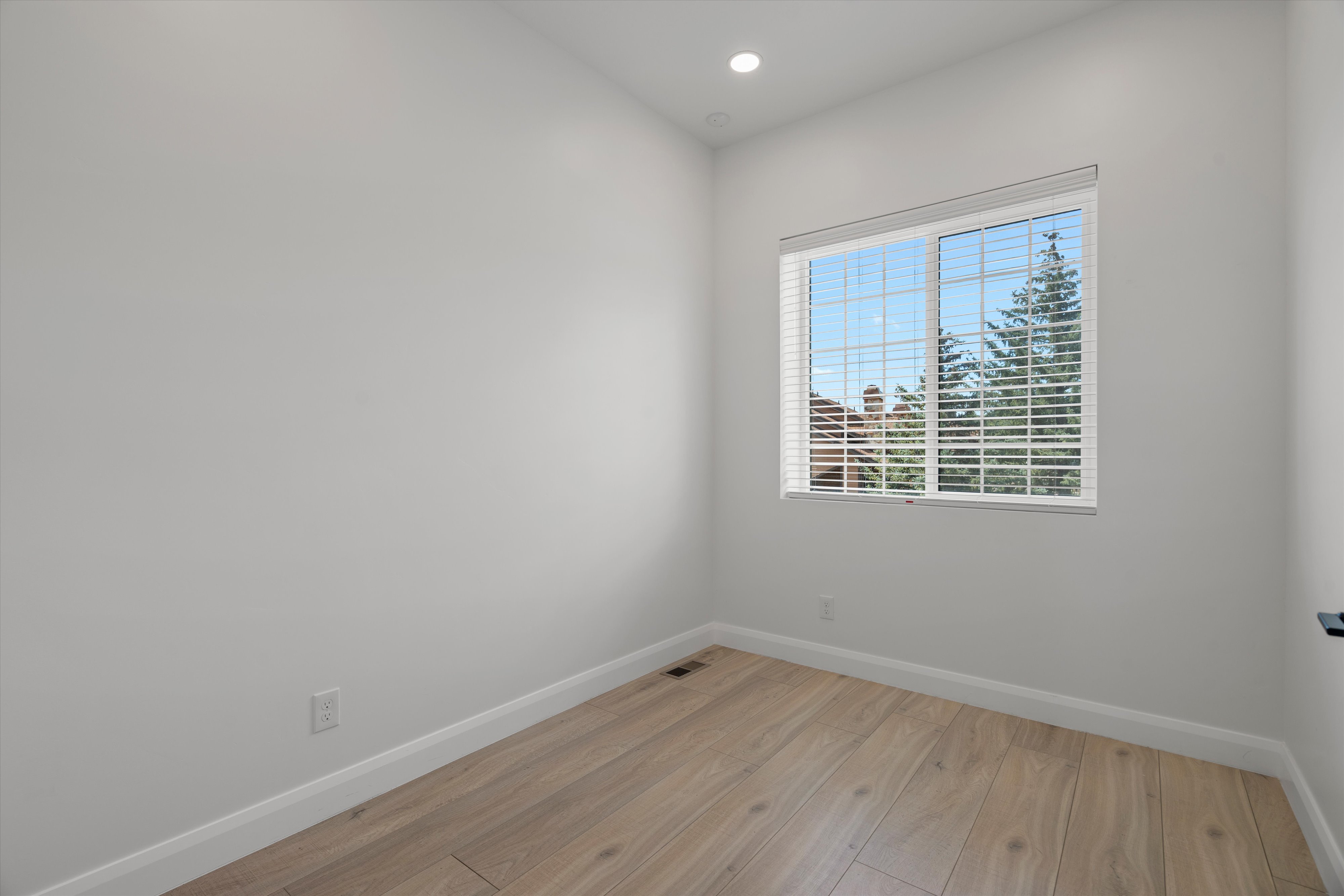Bright room with wood-finish flooring, white baseboards, a recessed ceiling light, and a window with horizontal blinds