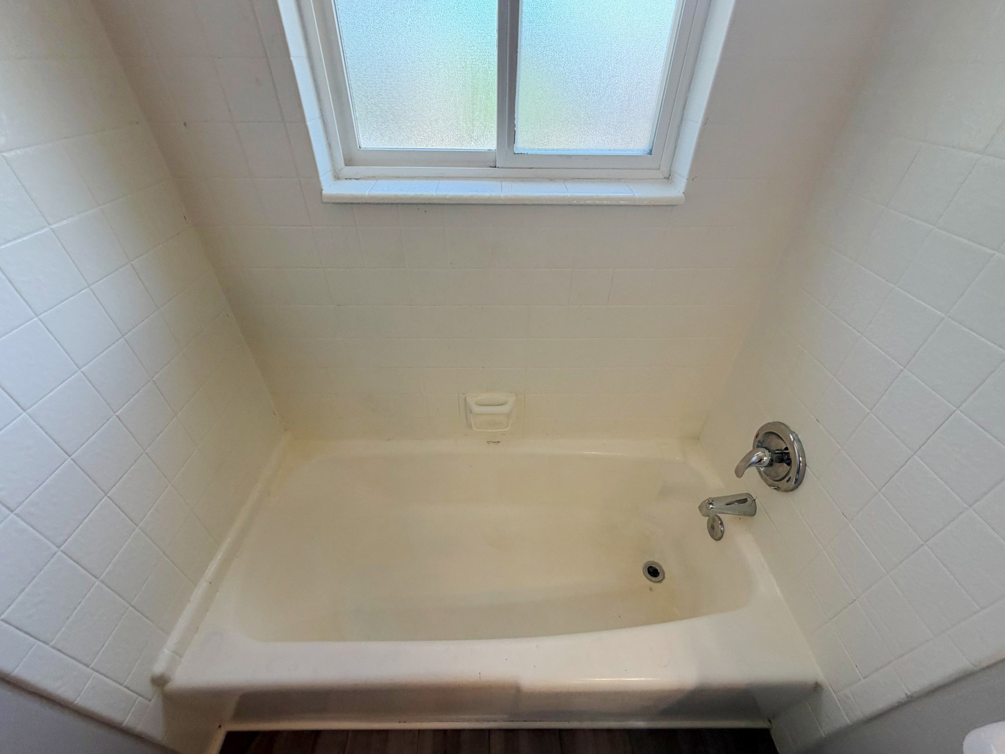 Bathtub with white tile surround and a frosted window