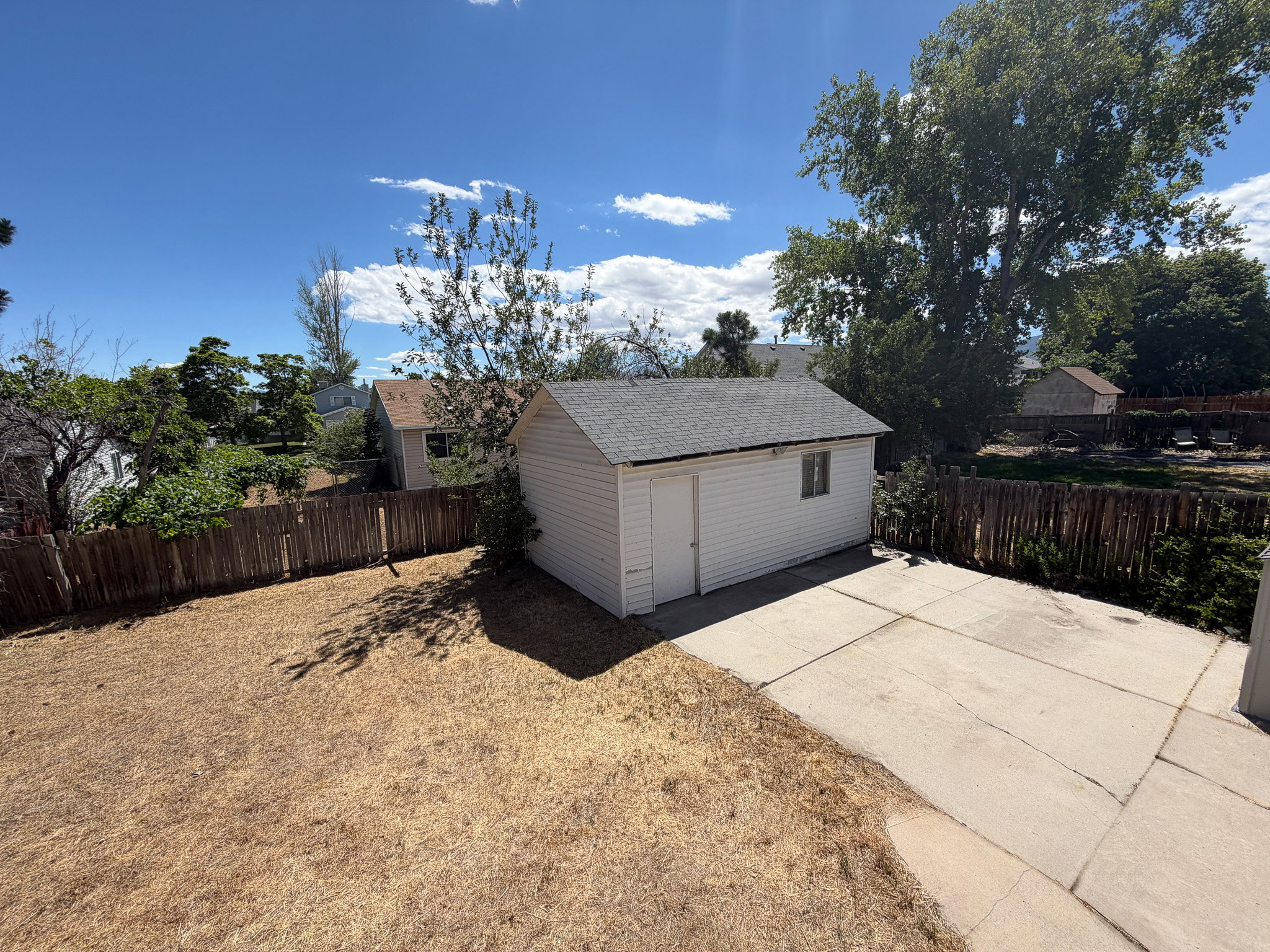 Detached white storage shed featuring a single door and window, situated on a concrete pad