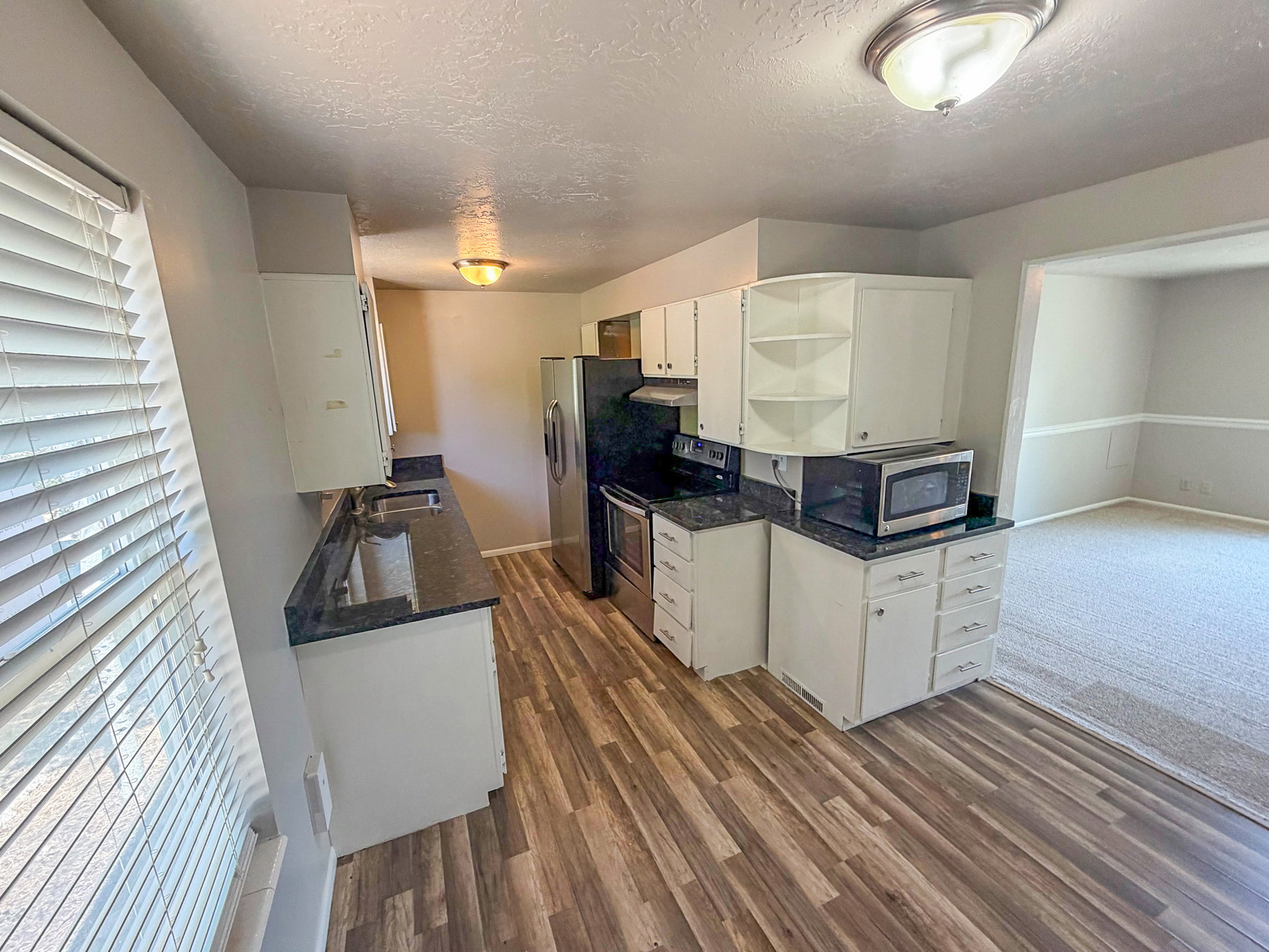 Kitchen featuring wood-finish flooring, white cabinetry, dark countertops, and stainless steel appliances