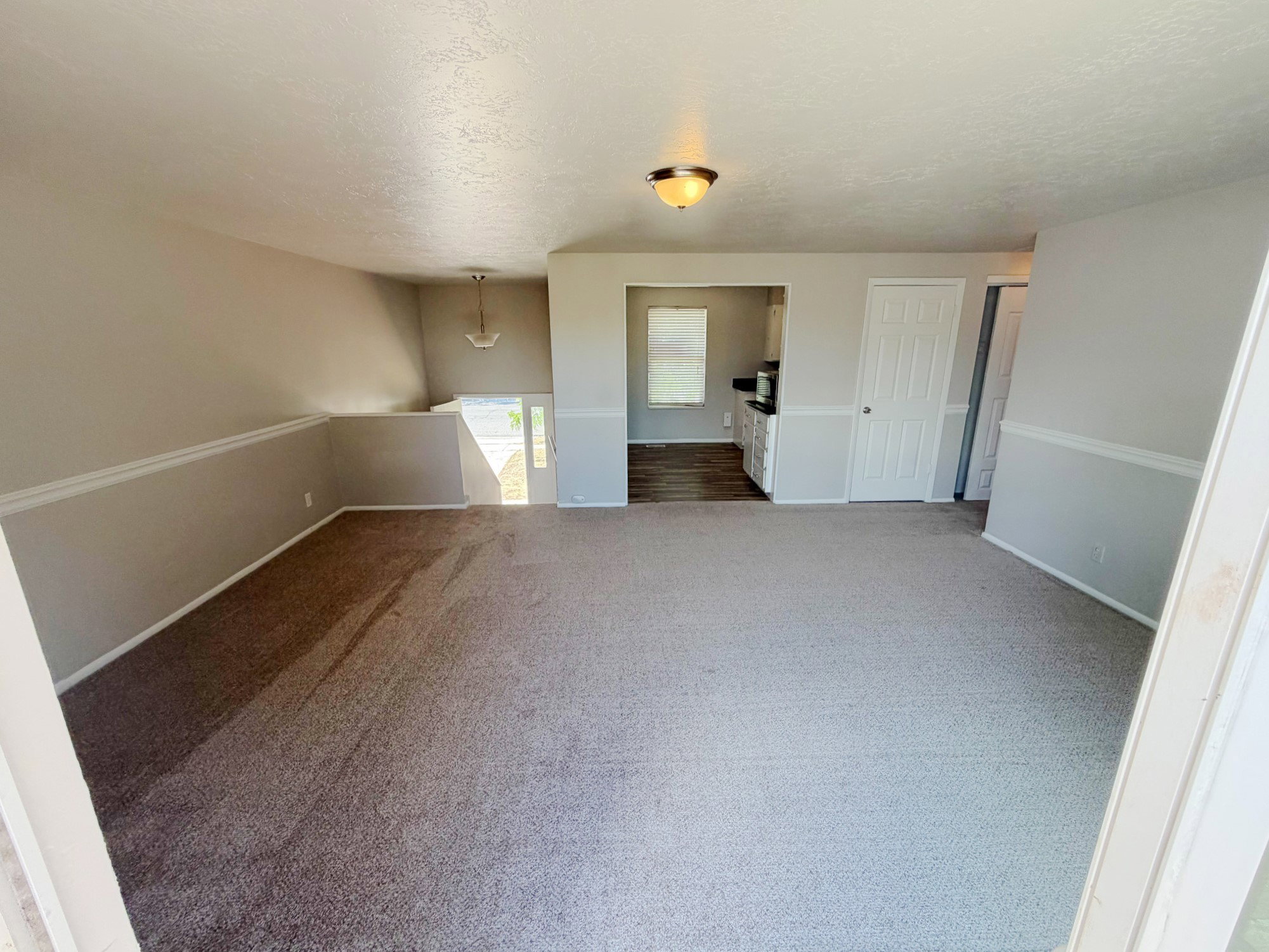 Spacious carpeted room featuring a neutral color palette, ceiling-mounted light fixture, and white trim