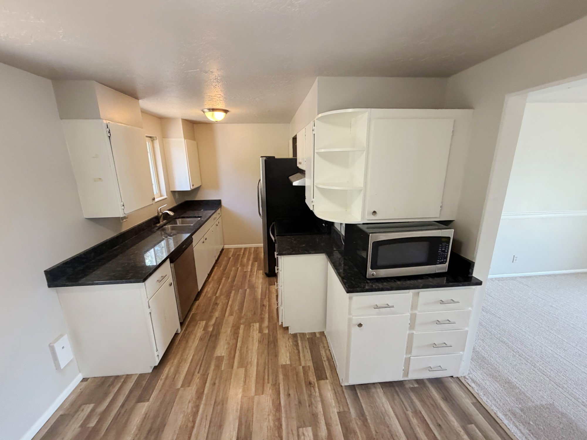 U-shaped kitchen featuring wood-finish flooring, white cabinetry, dark stone-finish countertops, and an undermount double-basin sink