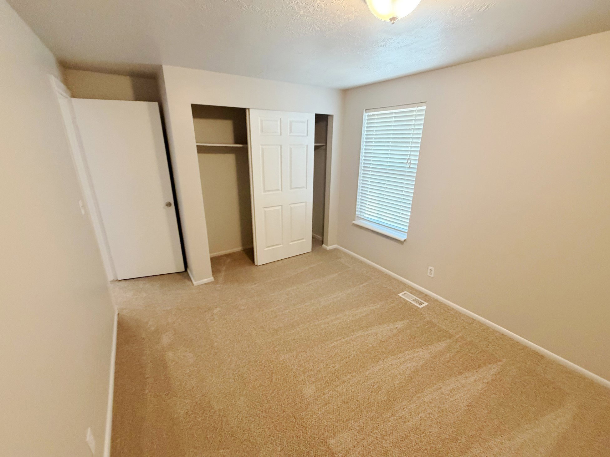 Neutral tone wall paint, carpeted flooring, and a window with horizontal blinds