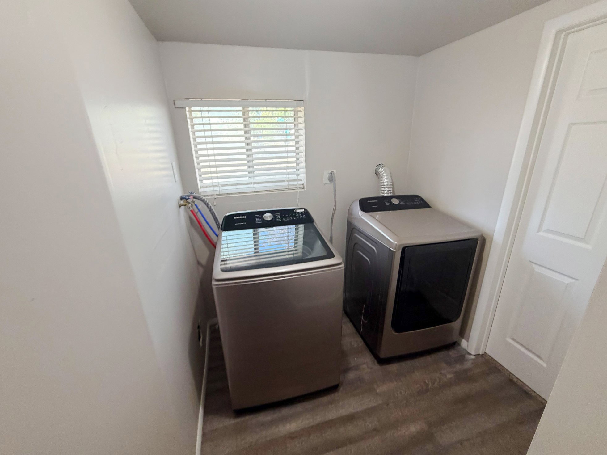 Dedicated laundry space featuring wood-finish flooring, a window with blinds, and white walls