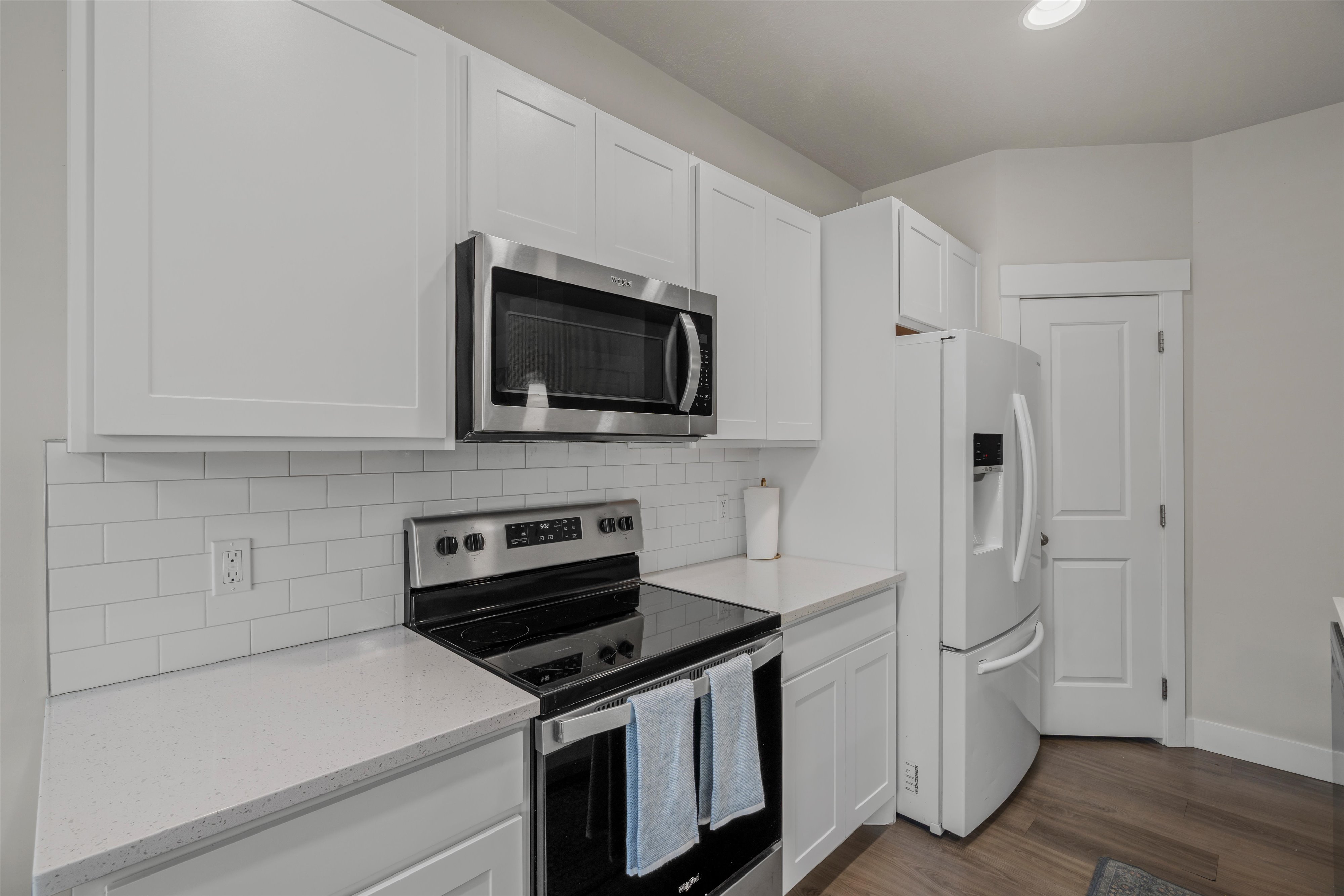 Kitchen featuring white shaker cabinetry, stainless steel microwave, black electric range, white subway tile backsplash, and light-toned countertops