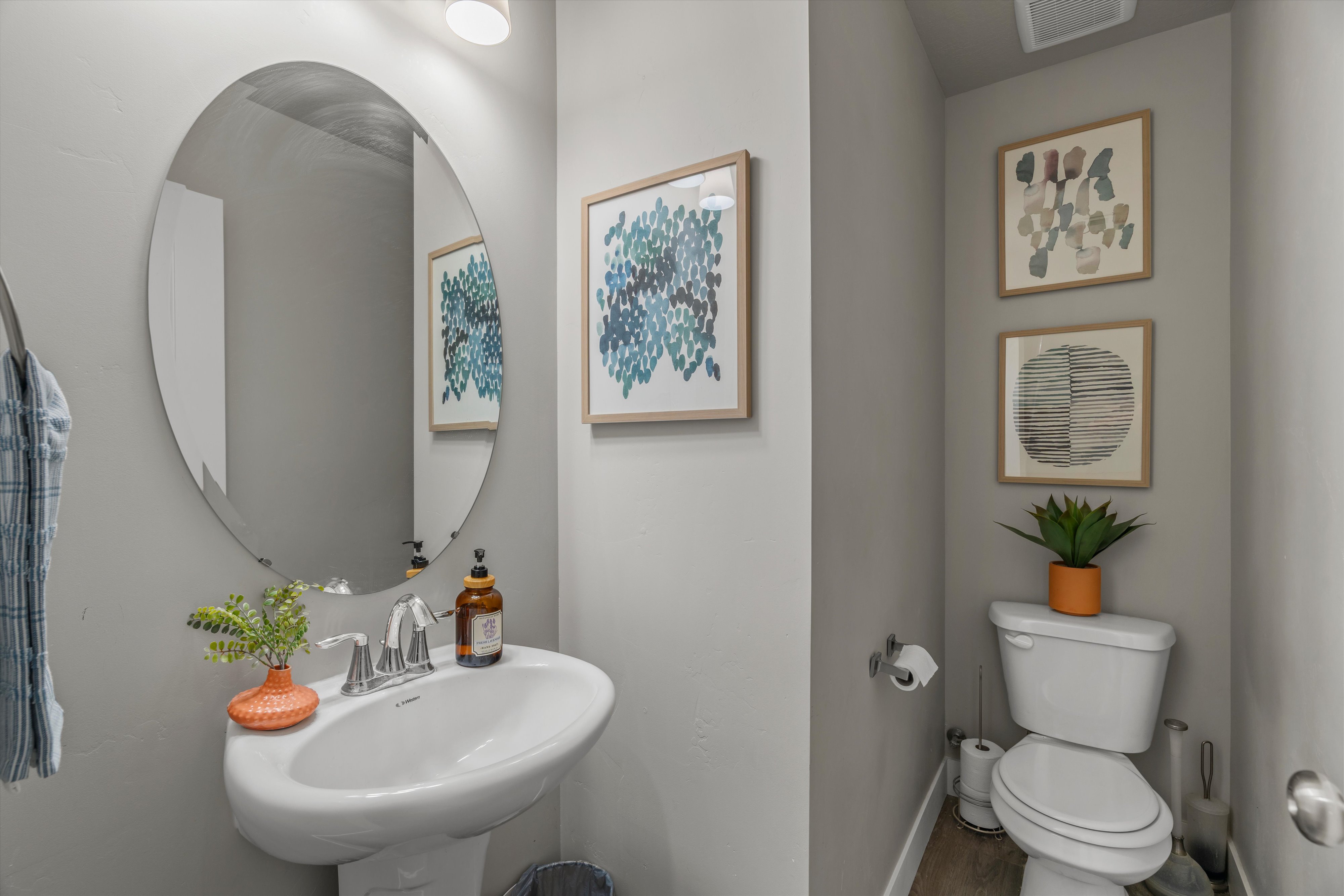 Pedestal sink with chrome faucet, complemented by an oval wall mirror