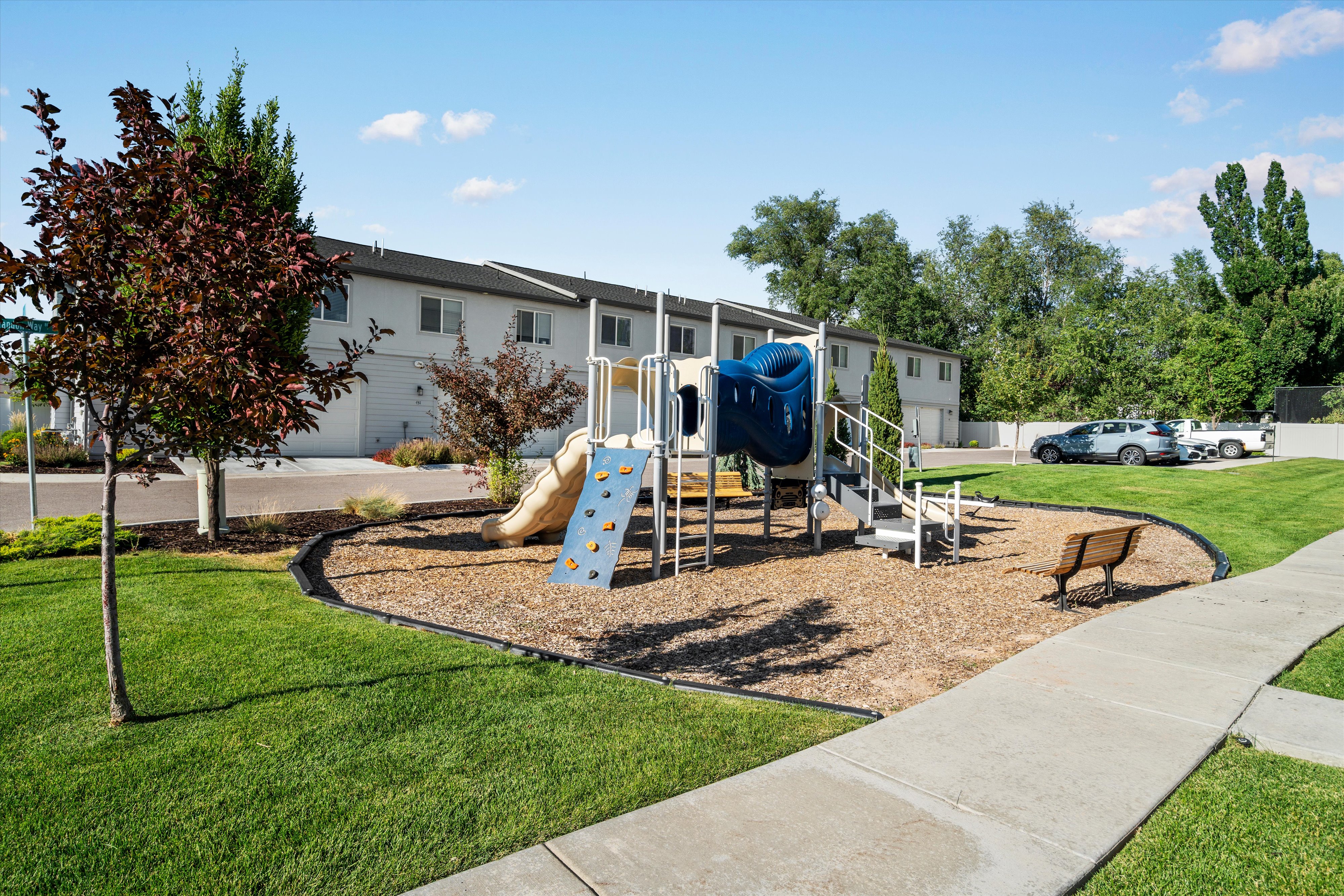 Community playground area featuring a multi-level structure with slides and climbing elements, surrounded by wood chips