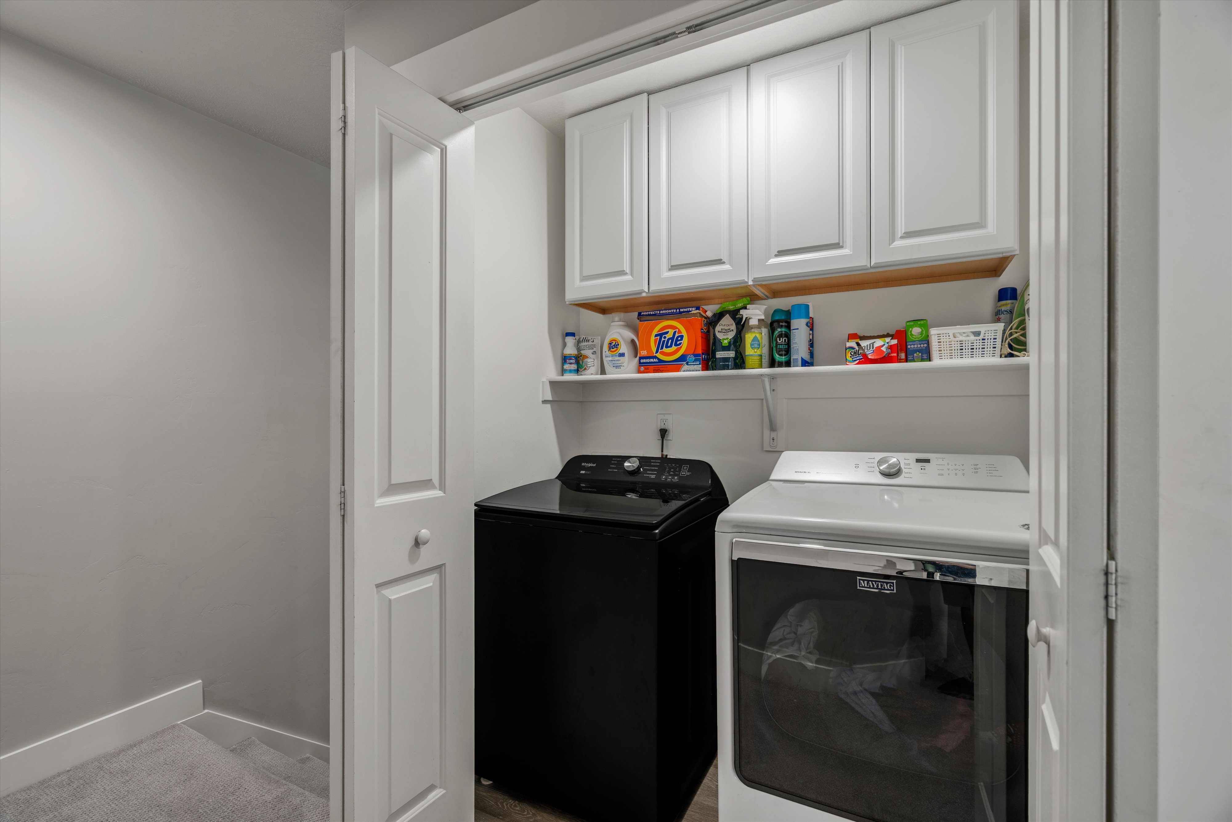 Dedicated laundry area featuring white shaker-style cabinetry, a built-in shelving unit, and a bifold door enclosure