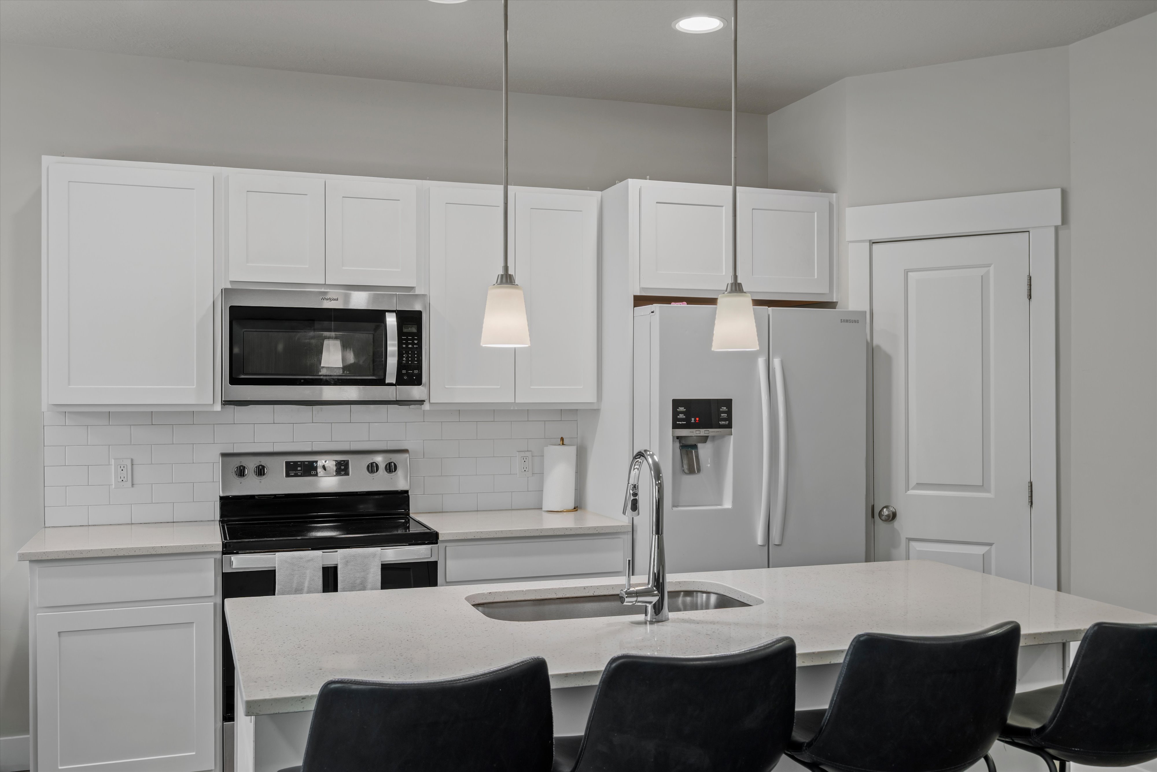 Kitchen featuring white cabinetry, stainless steel appliances, a white subway tile backsplash, a countertop island with seating, and pendant lighting