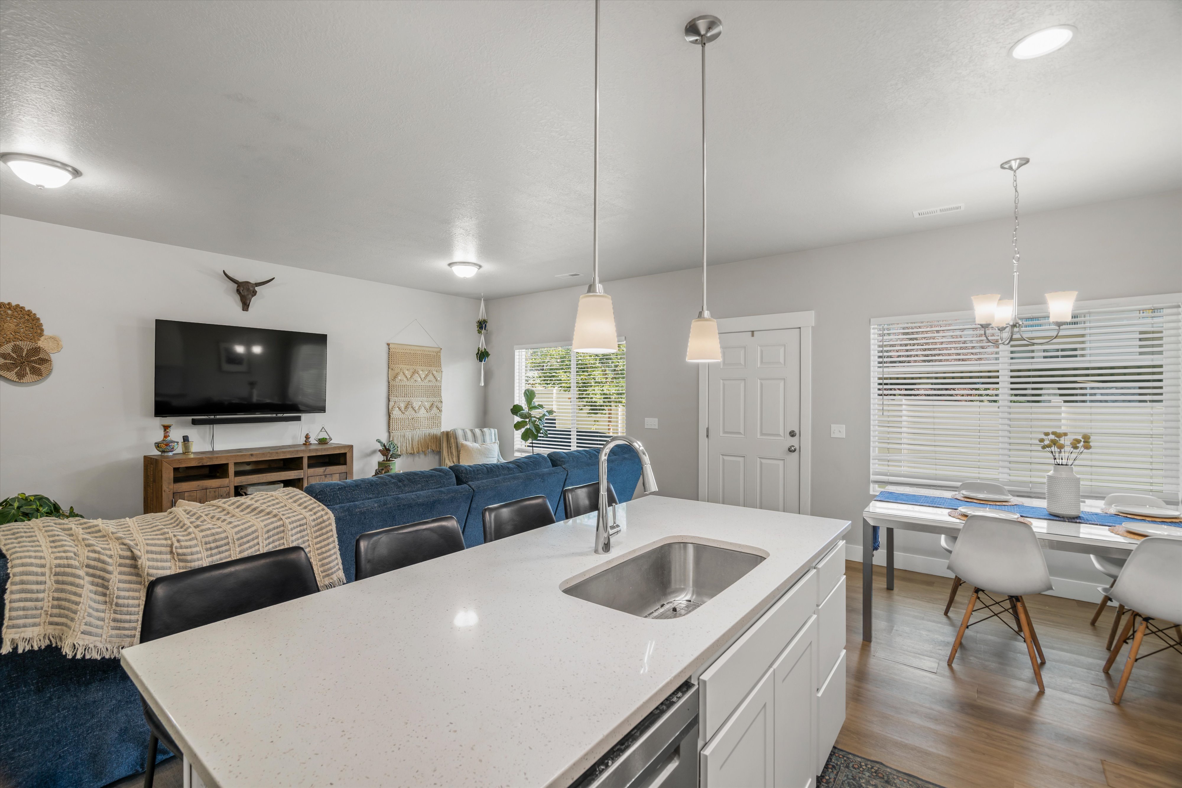 Open-concept living area featuring a kitchen island with an undermount sink and pendant lighting, wood-finish flooring, and a dining space with a chandelier
