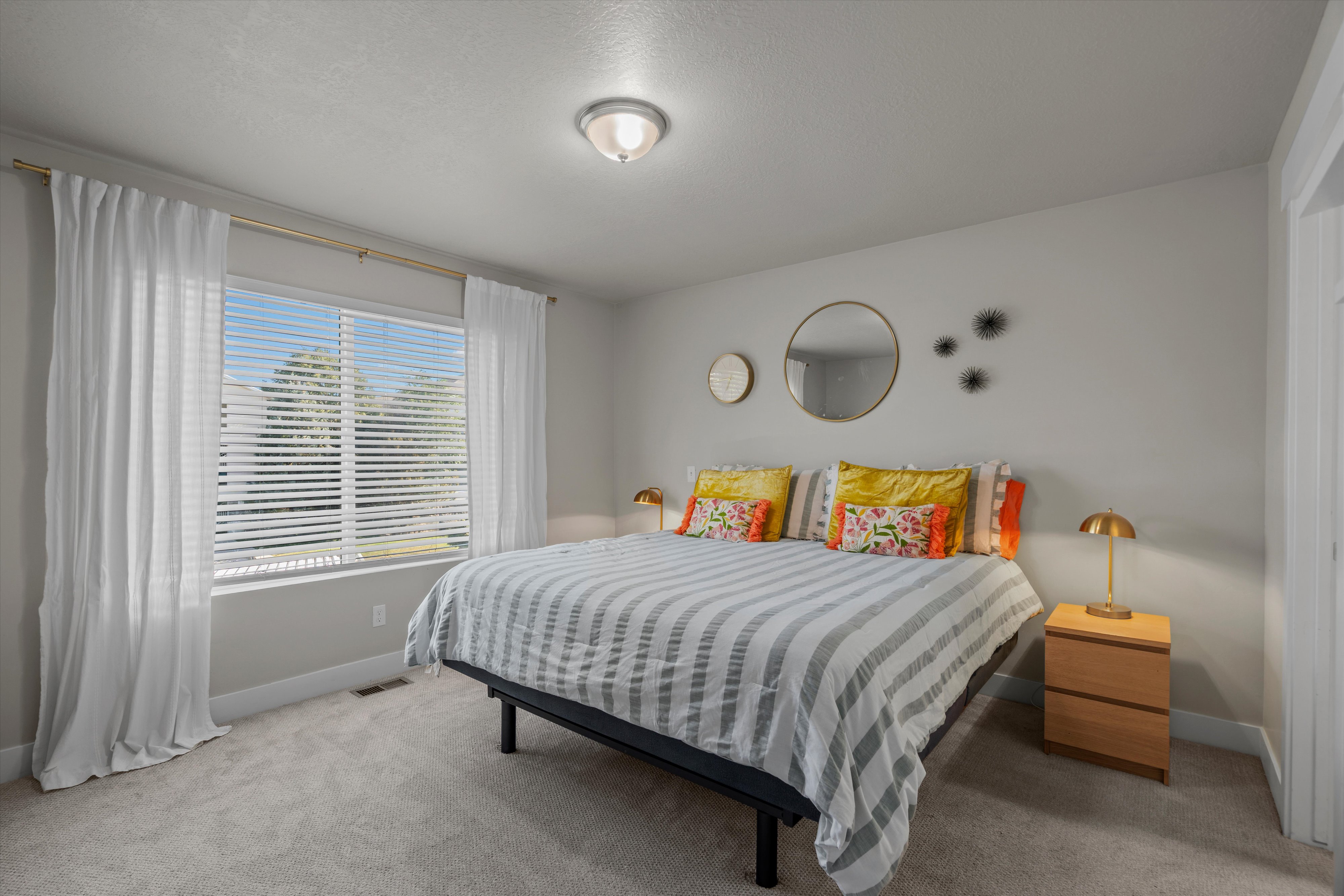Bedroom featuring soft gray carpeting, a large window with white blinds, and a flush-mount ceiling light fixture