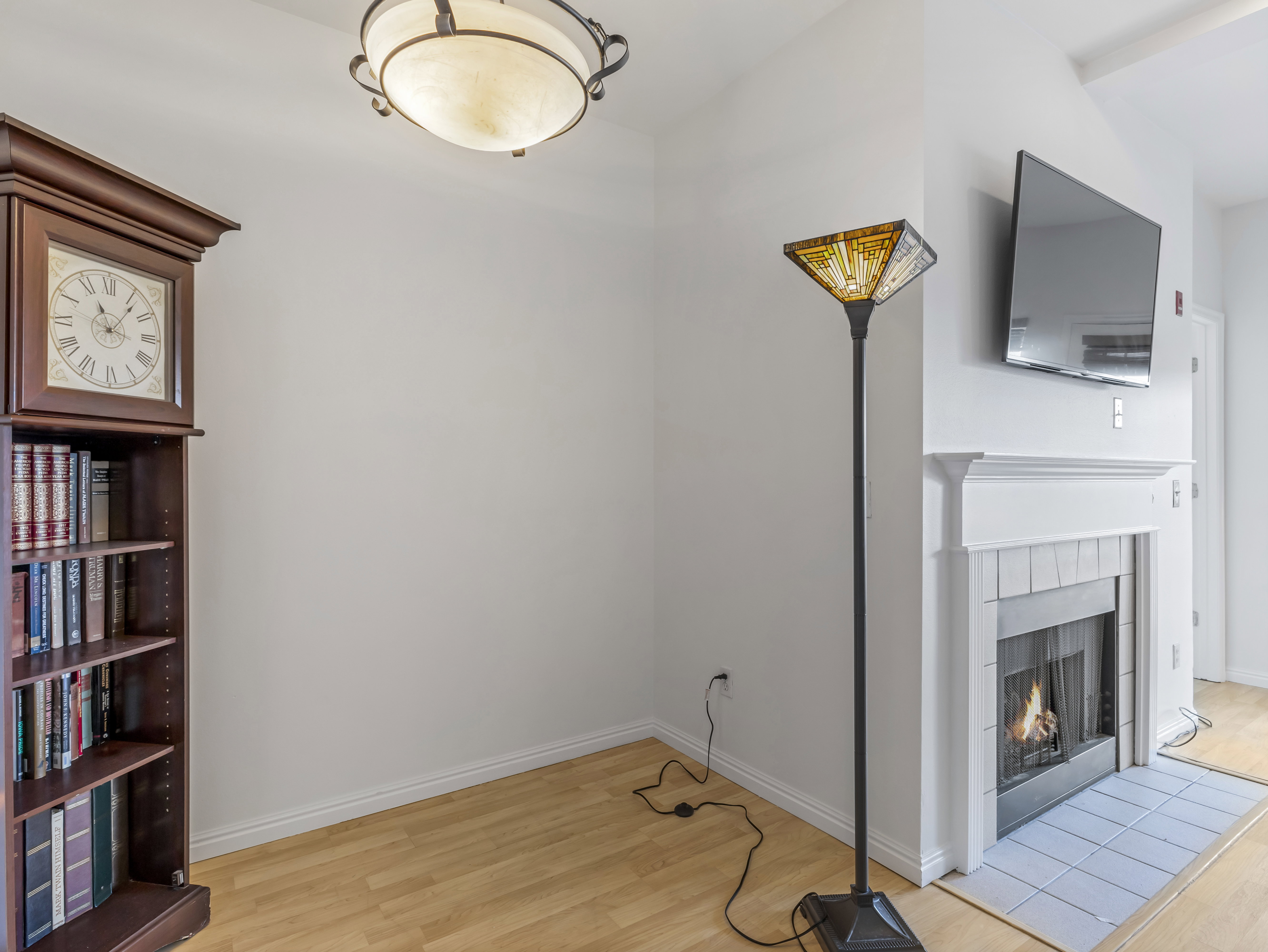 Fireplace with white tile surround and mantelpiece, light wood-finish flooring, and white baseboards