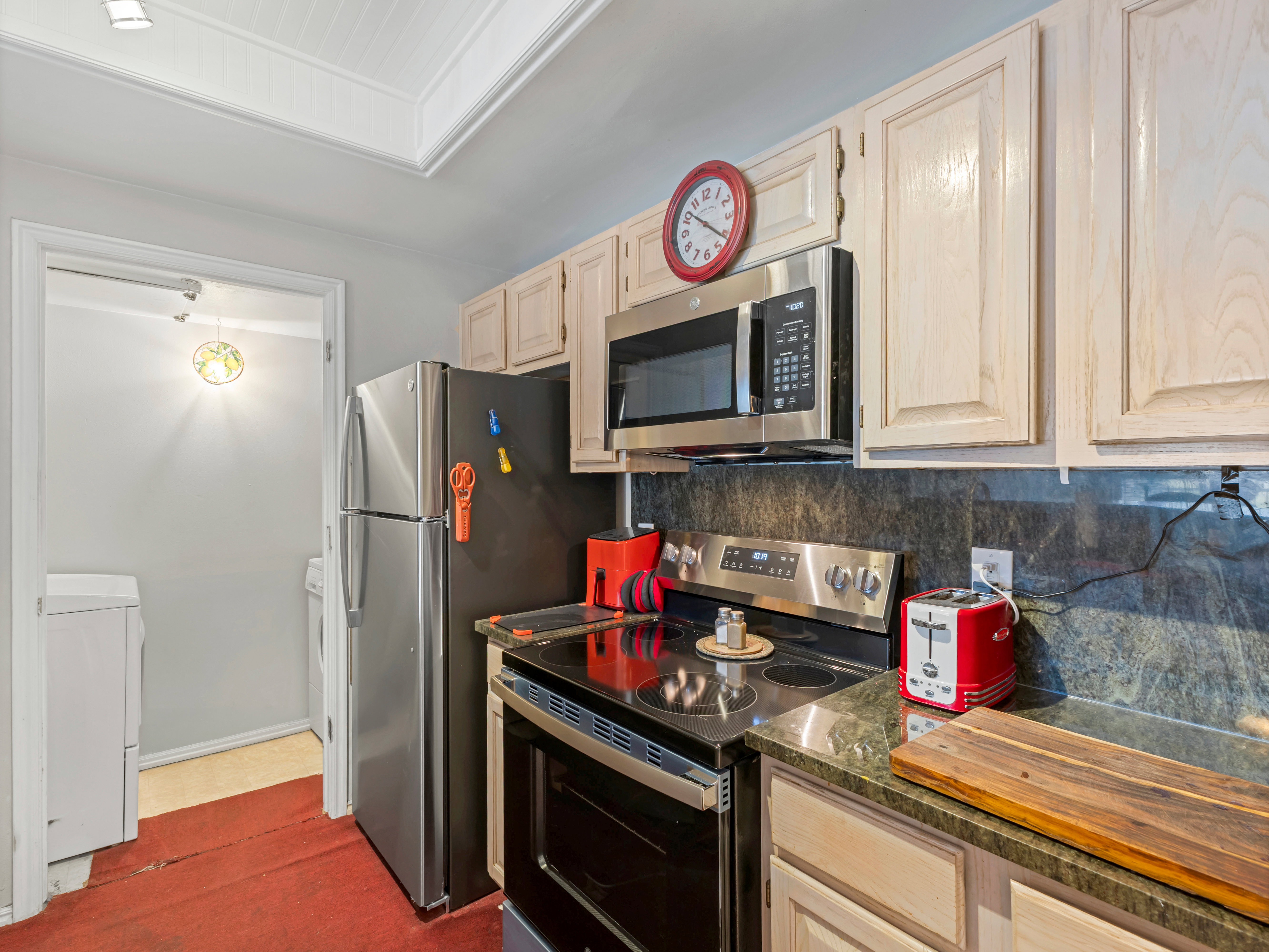 Kitchen featuring light-toned cabinetry, stainless steel appliances, dark stone countertops, and a full-height stone backsplash