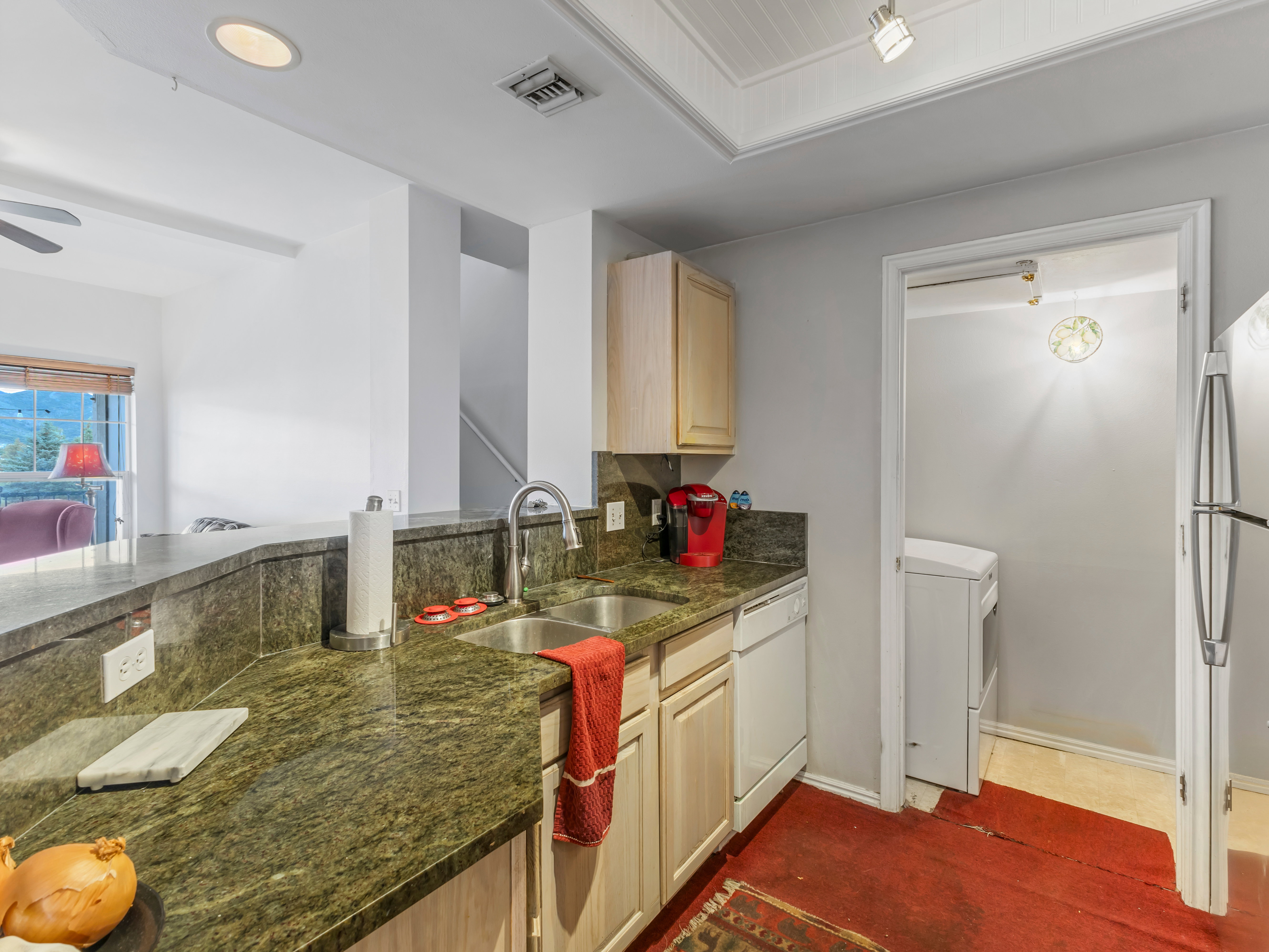 Kitchen featuring a double basin stainless steel sink, wood-finish cabinetry, built-in dishwasher, and a breakfast bar with stone-finish countertops