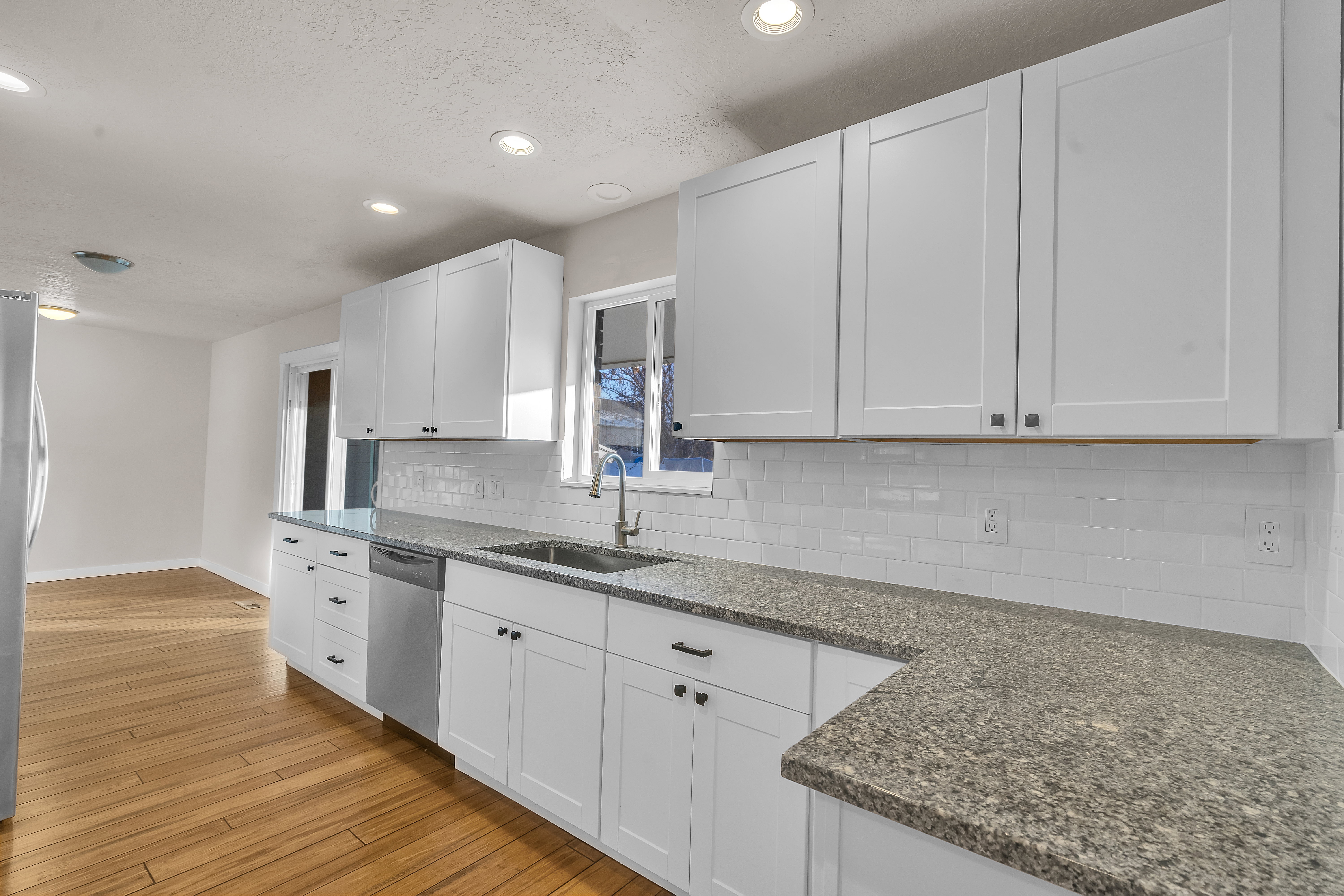 Kitchen featuring white shaker-style cabinetry, granite-finish countertops, subway tile backsplash, stainless steel sink, and wood-finish flooring