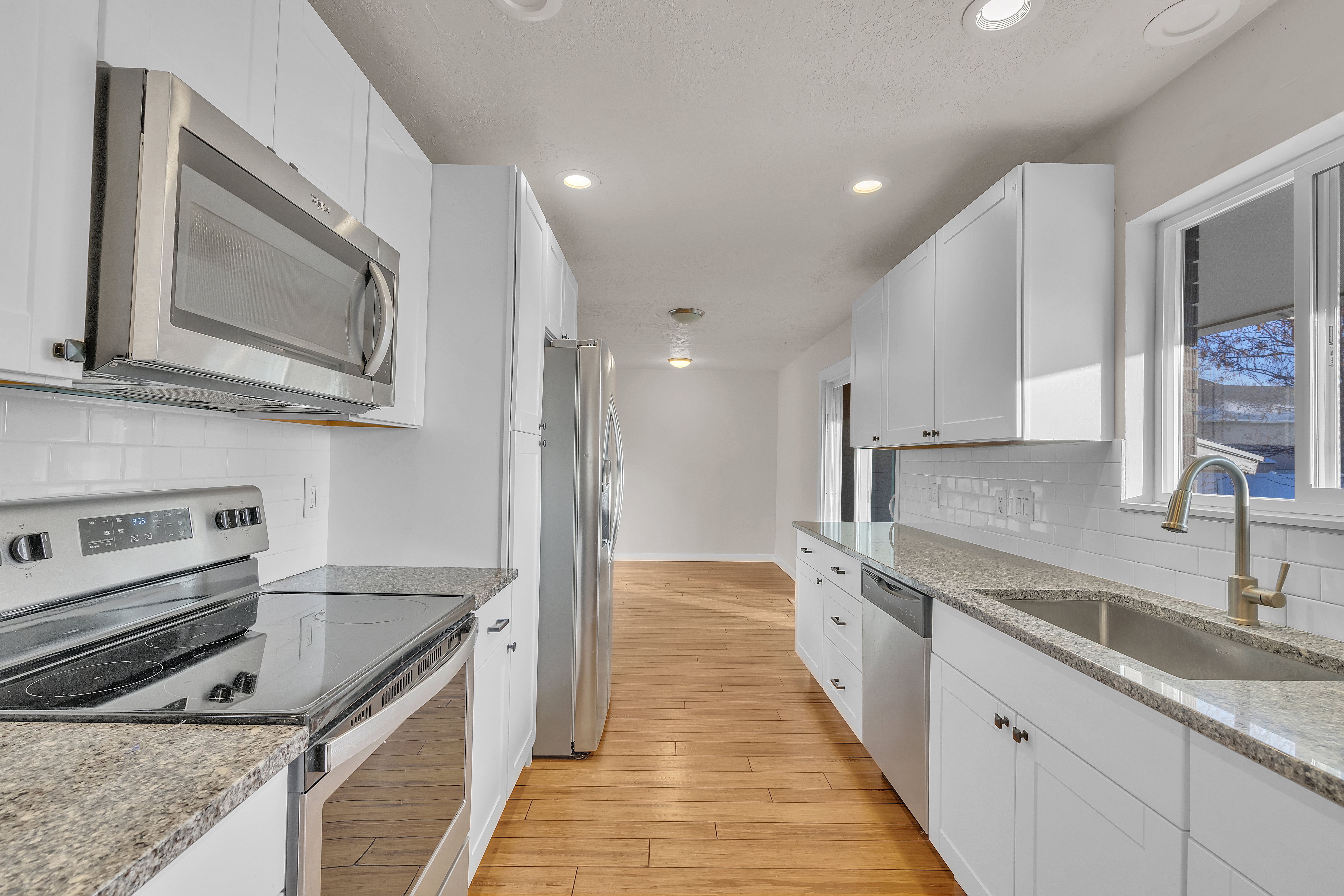 Kitchen featuring wood-finish flooring, white cabinetry, granite countertops, and stainless steel appliances including a built-in microwave, range, and refrigerator