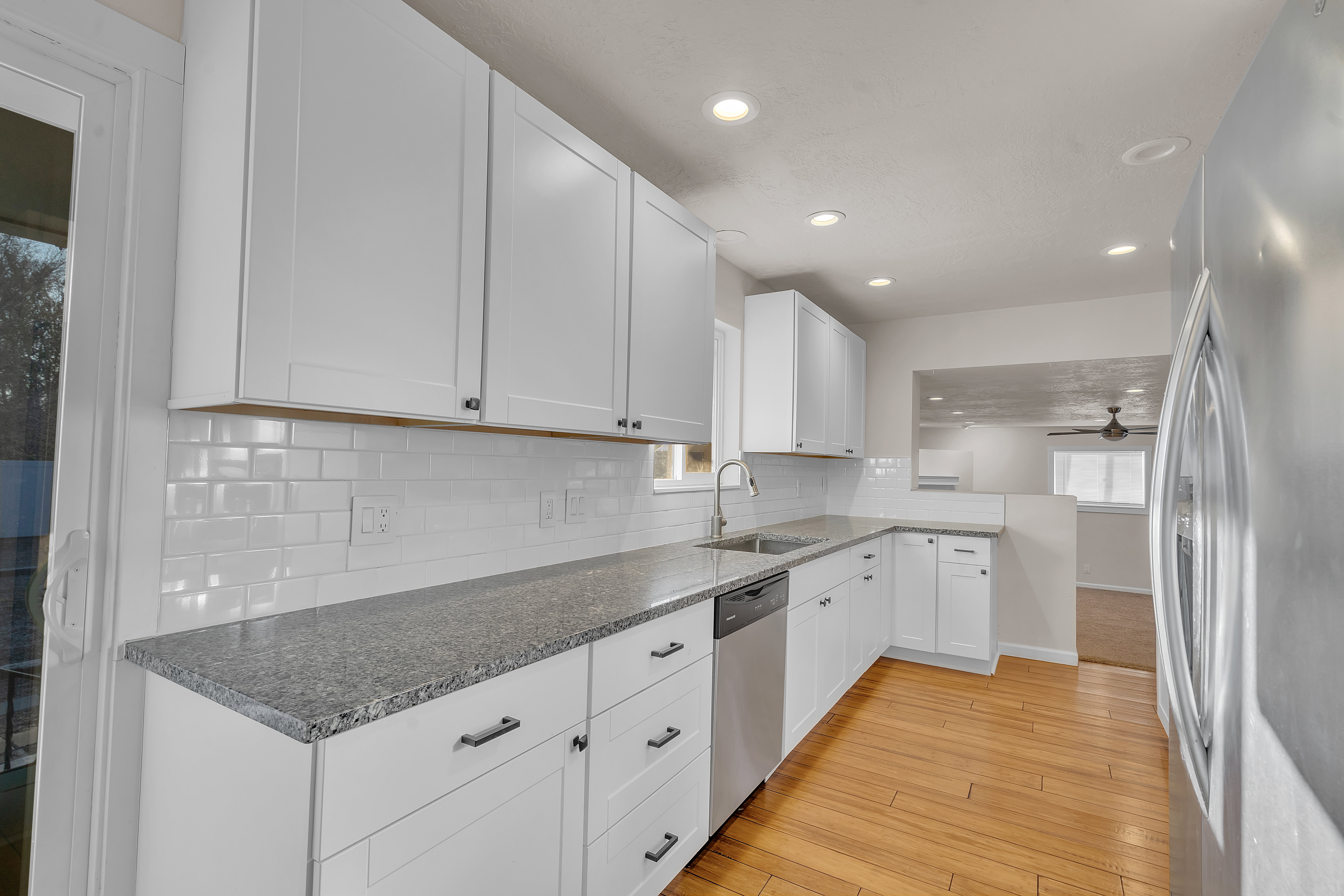 Kitchen featuring white shaker cabinetry, speckled countertops, a white subway tile backsplash, stainless steel appliances, and wood-finish flooring
