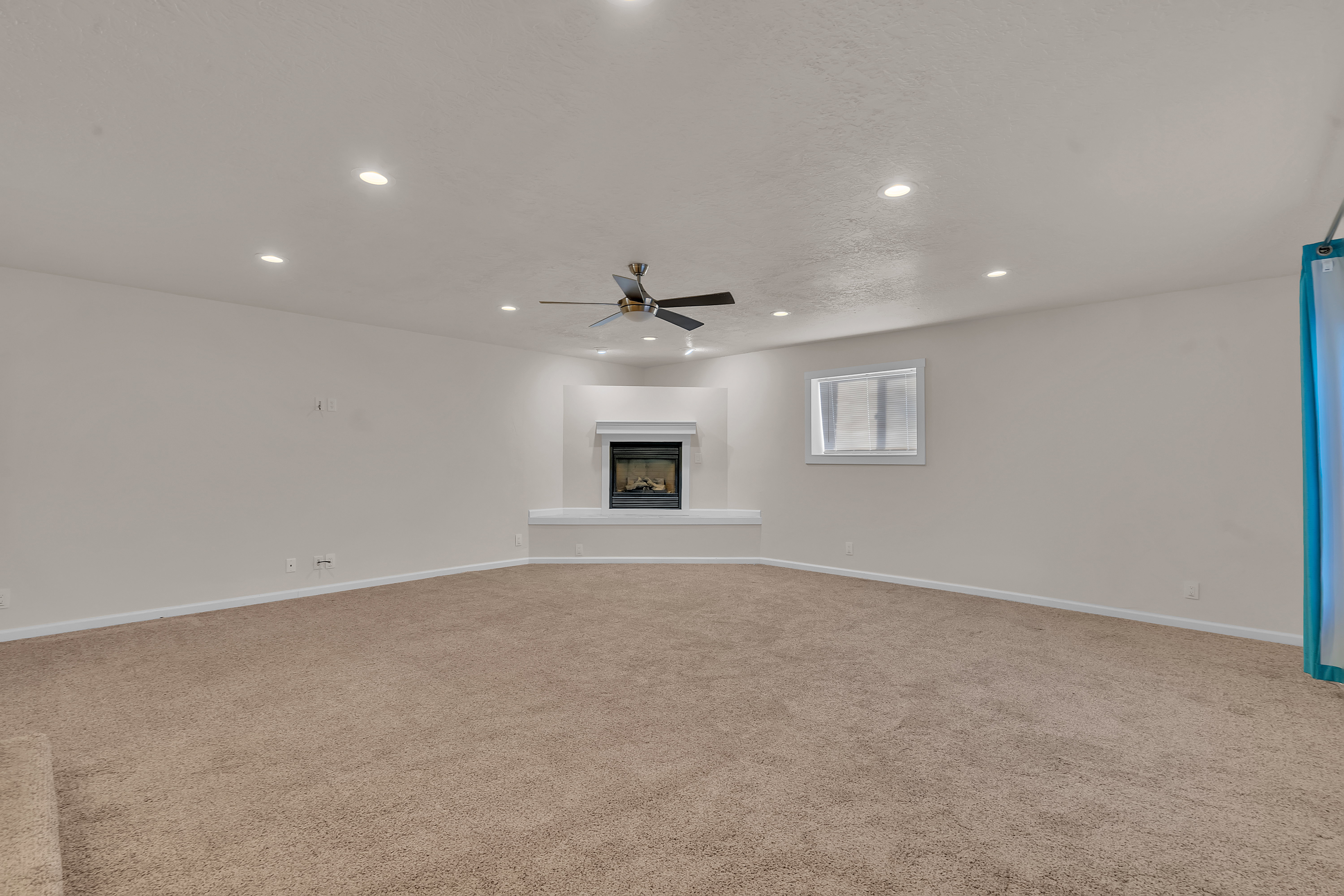 Spacious room featuring a corner fireplace with a white mantel, recessed lighting, and a ceiling fan