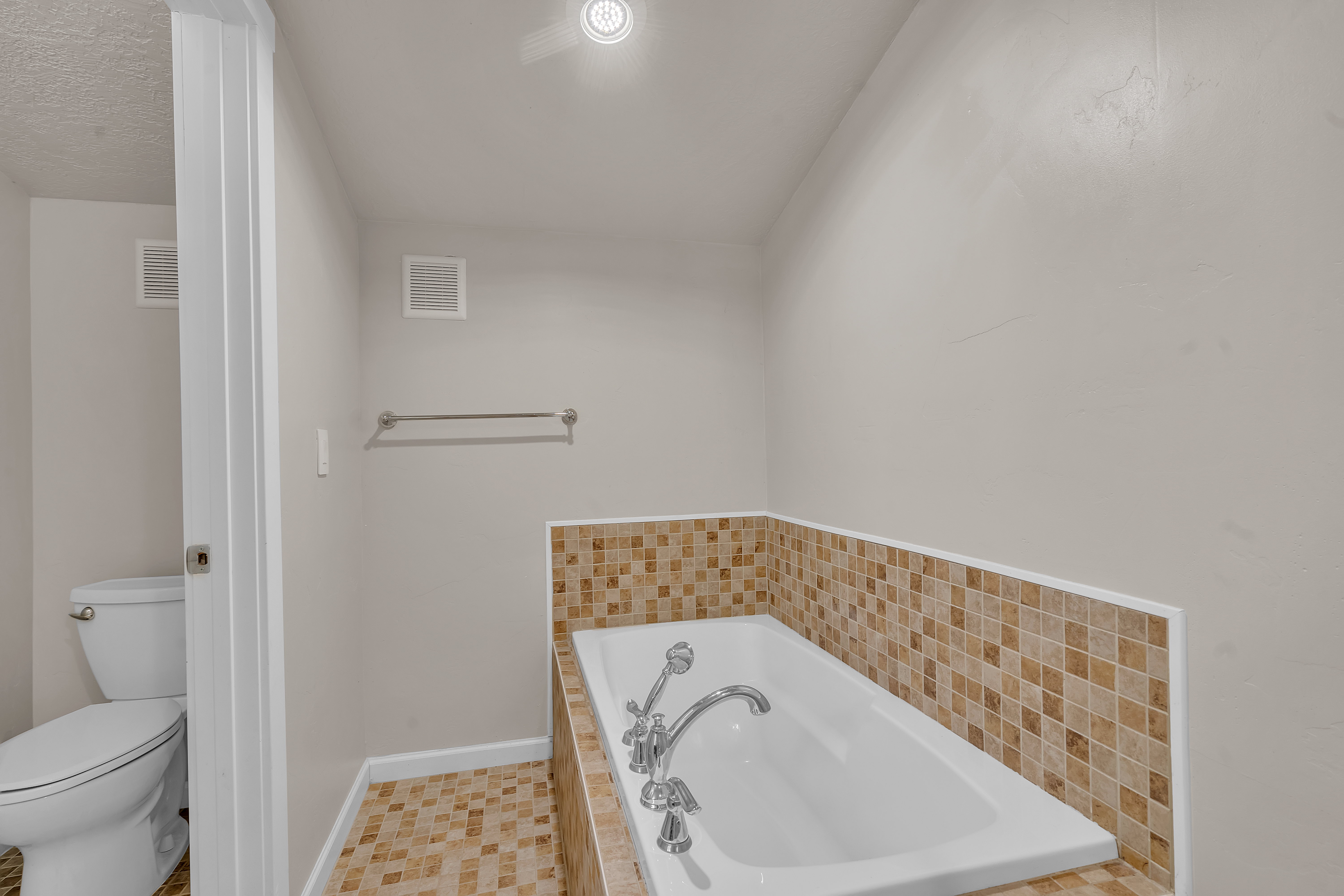 Soaking tub with mosaic tile surround, chrome fixtures, and complementary tile flooring