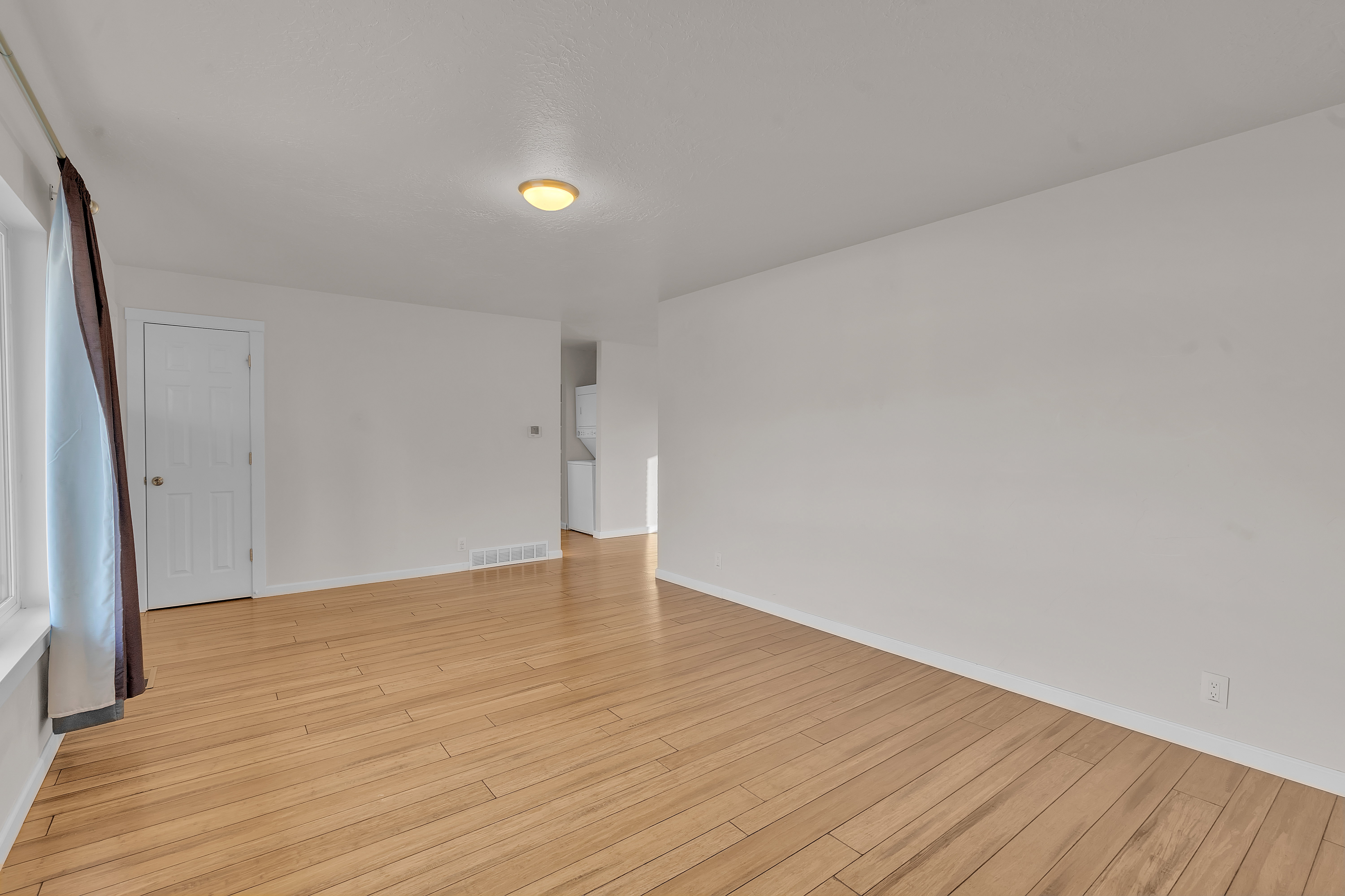 Spacious interior room featuring wood-finish flooring, white walls, and a recessed ceiling light fixture