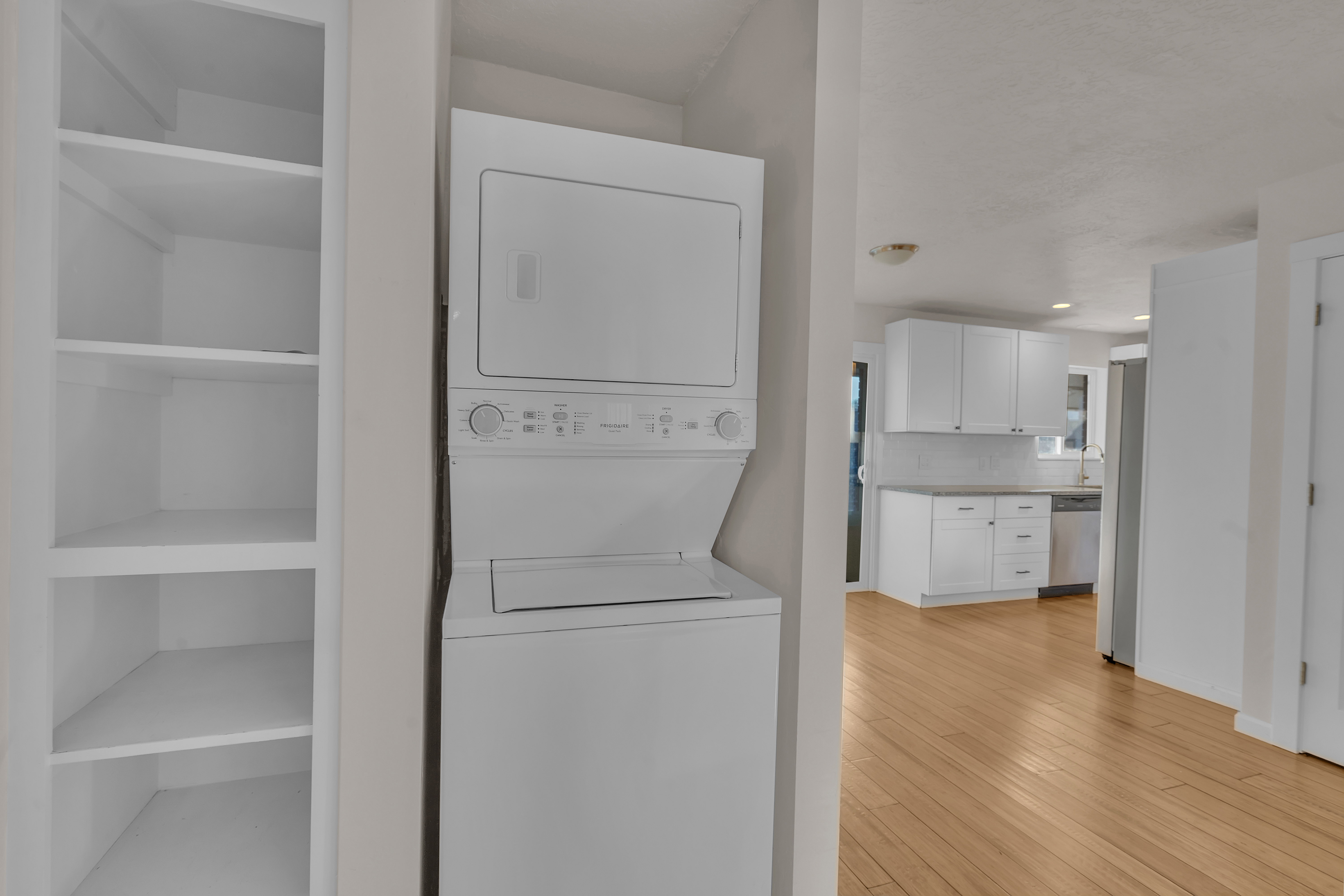 Laundry area featuring a stacked washer and dryer, adjacent to white built-in shelving