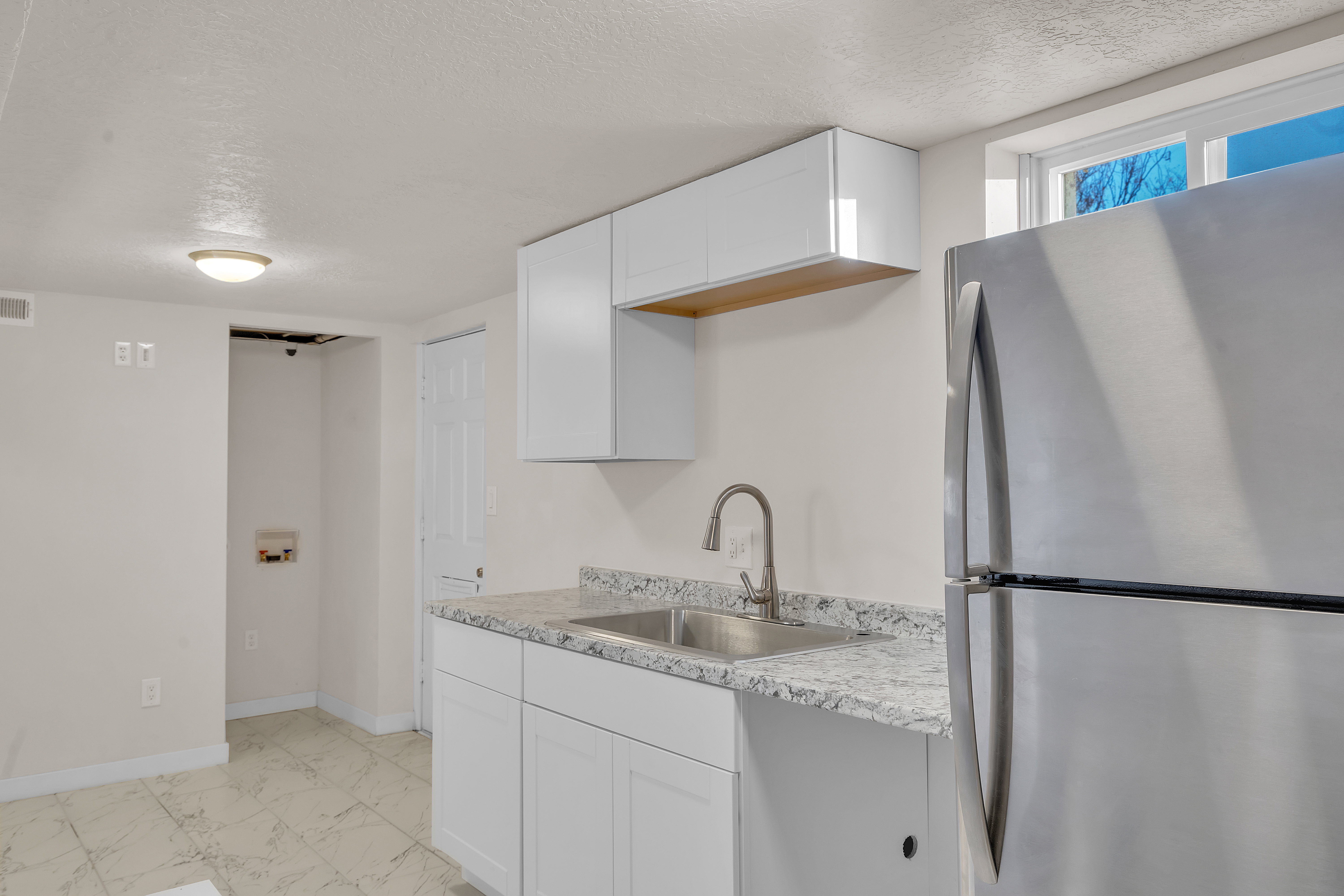 Kitchenette featuring stainless steel refrigerator, white shaker-style cabinetry, granite-finish countertops, and a stainless steel sink with a gooseneck faucet