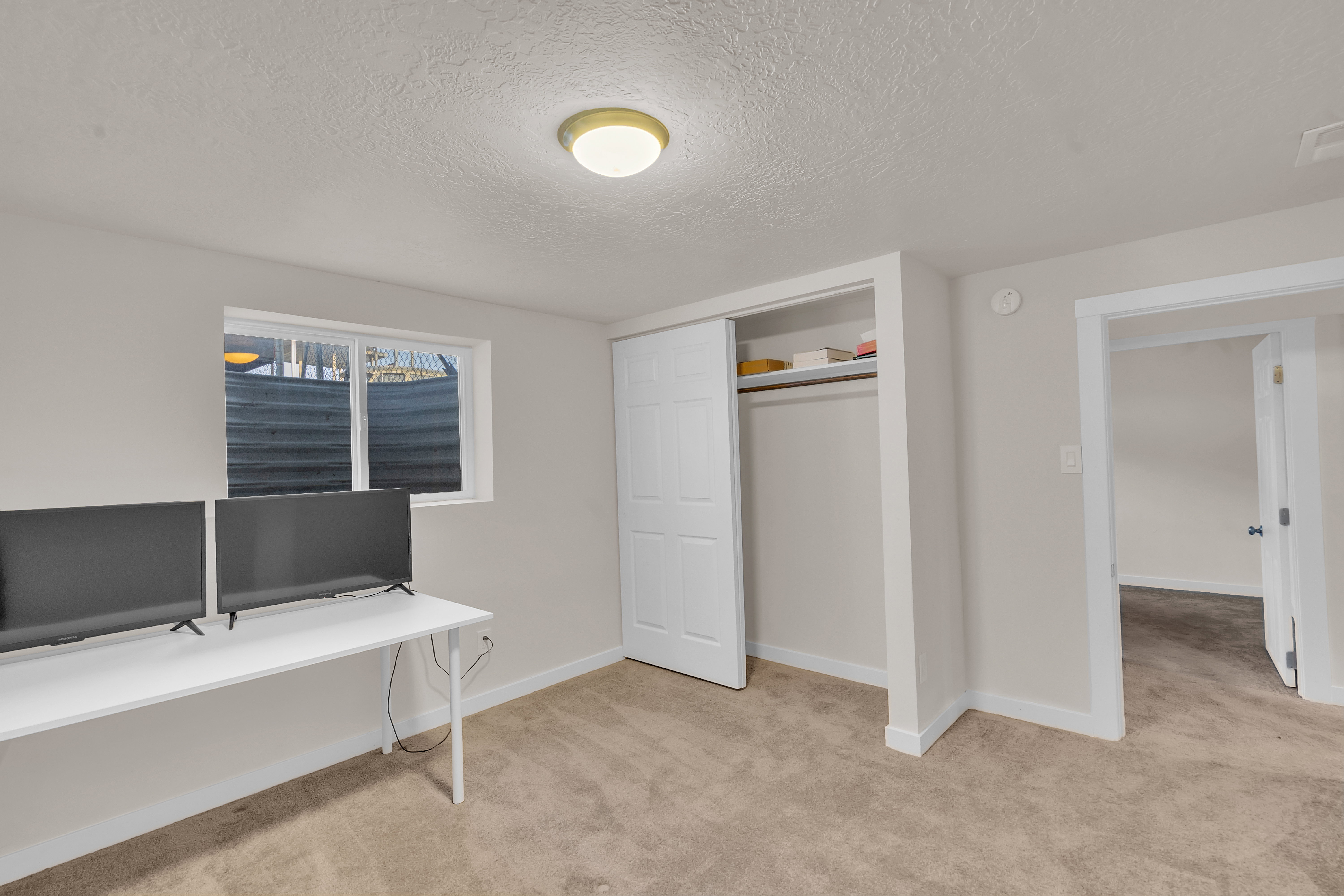Carpeted room featuring a white-framed window, recessed closet with sliding doors, neutral wall paint, and a flush mount ceiling light