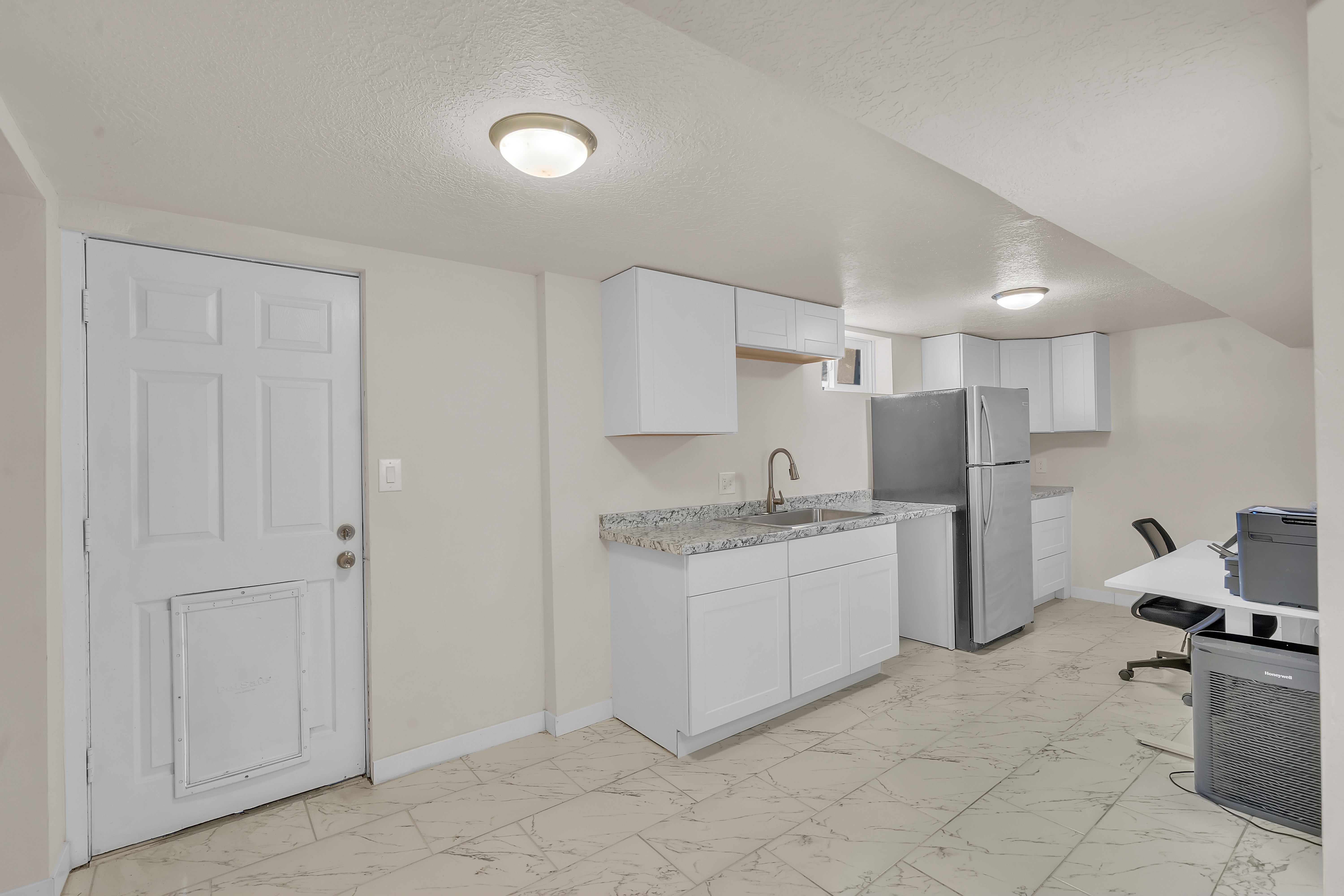 Kitchenette featuring white cabinetry, a stainless steel sink with a high-arch faucet, a stainless steel refrigerator, and granite-finish countertops