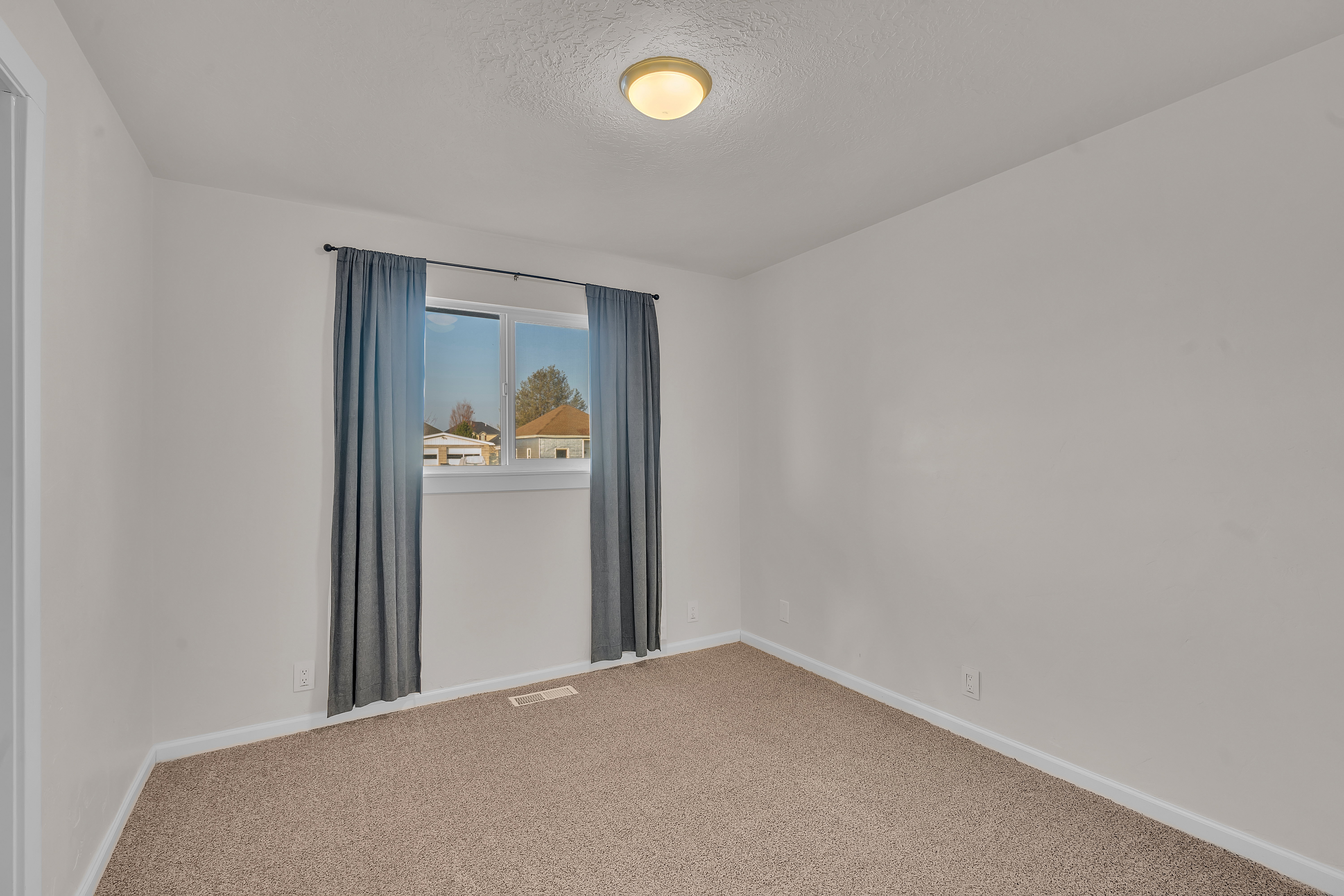 Carpeted interior room with white walls, a single window featuring dark blue drapes, and a flush-mount ceiling light fixture