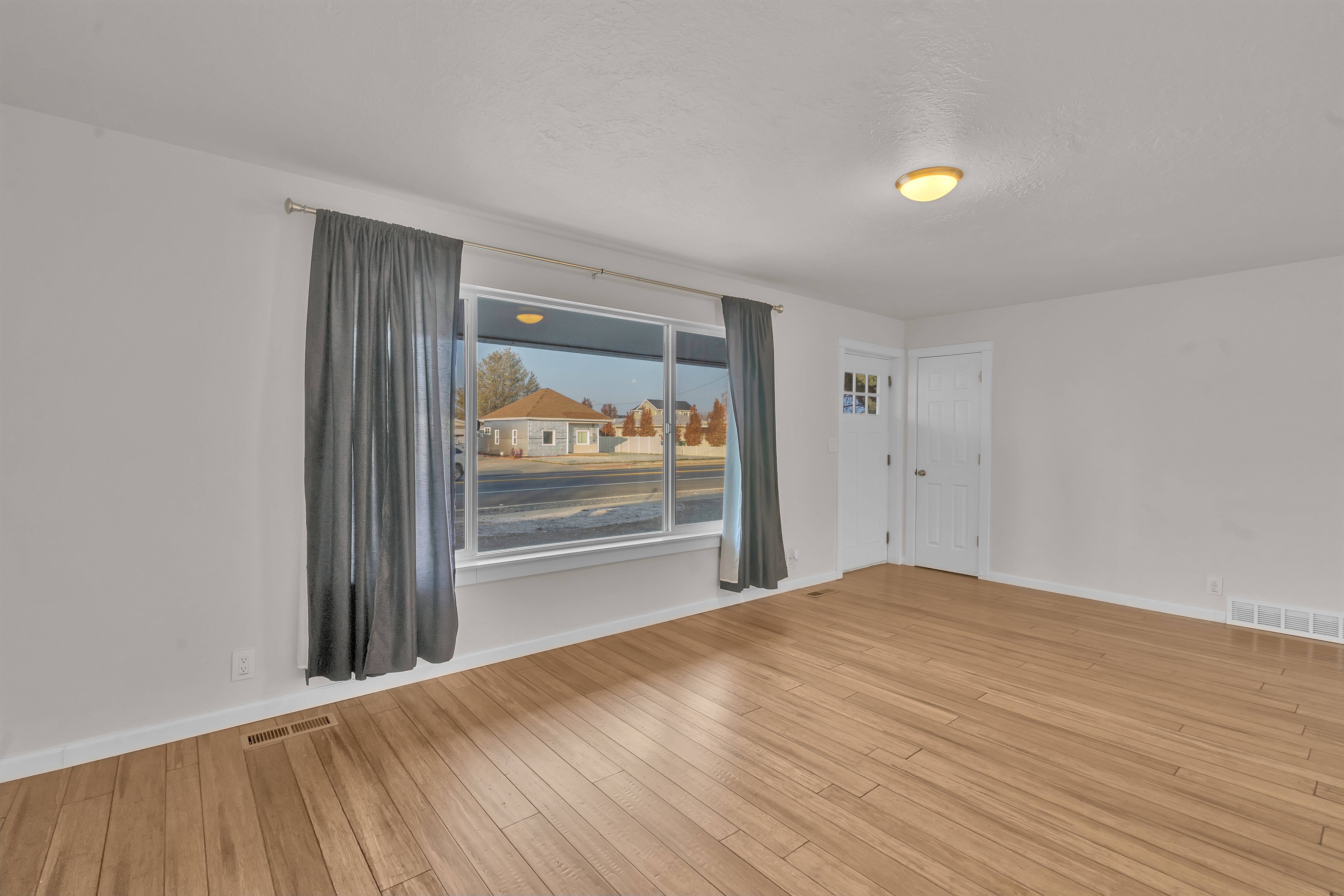 Spacious room featuring wood-finish flooring, white walls, and a large window