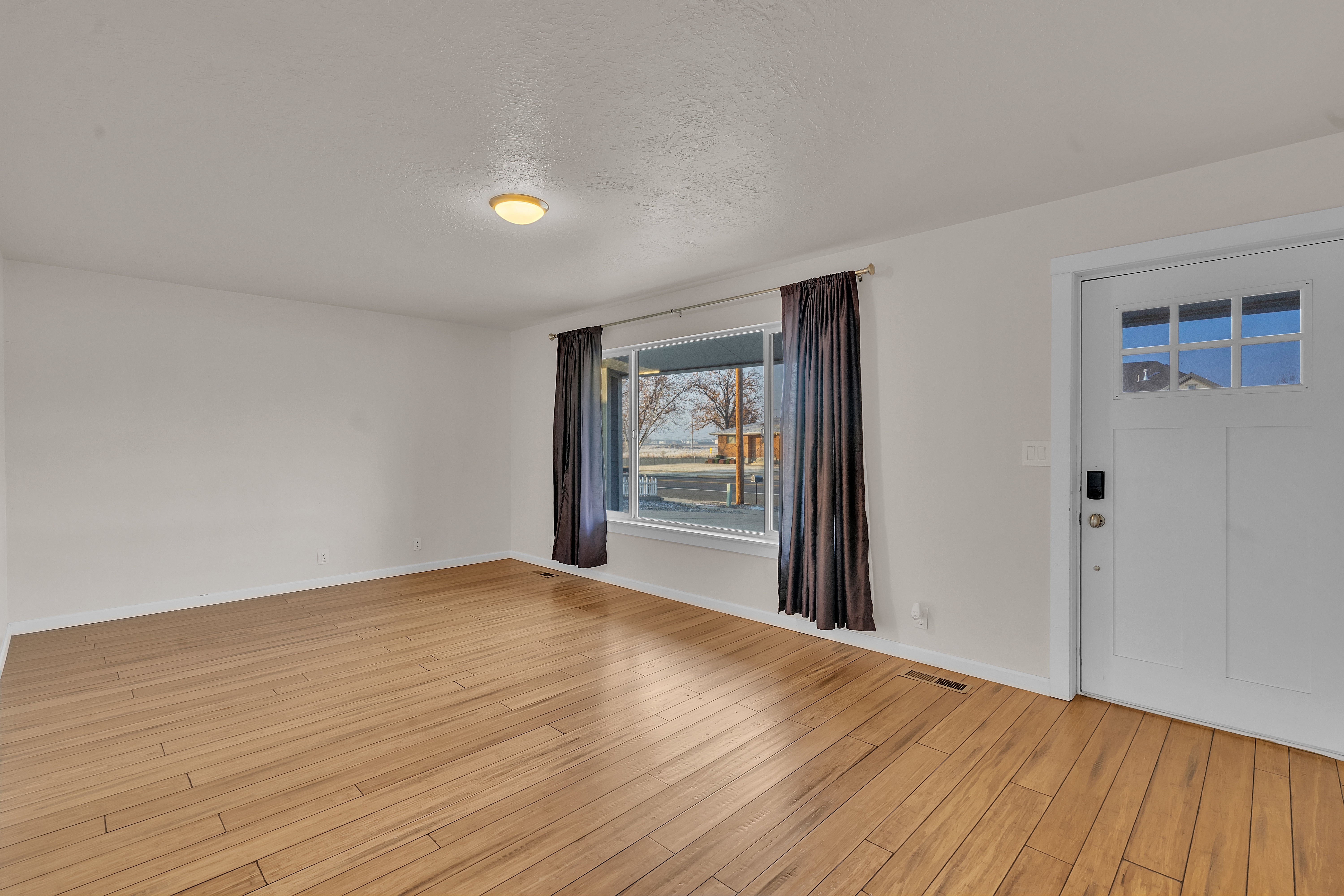 Expansive room featuring wood-finish flooring, a large window, a ceiling-mounted light fixture, and a white entry door with frosted glass panels