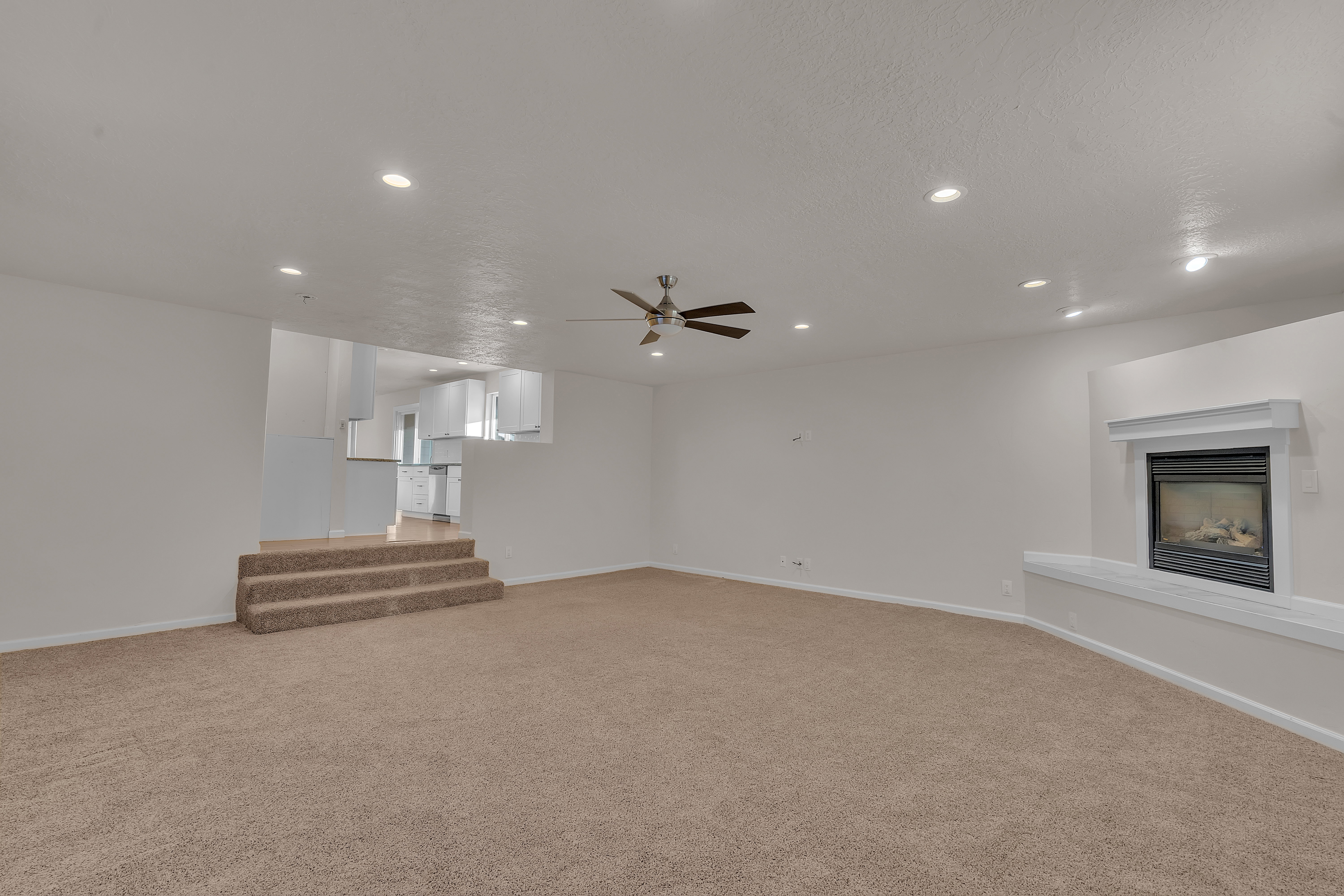Spacious living area featuring neutral carpeting, recessed lighting, a ceiling fan, and a built-in fireplace with a mantel and hearth