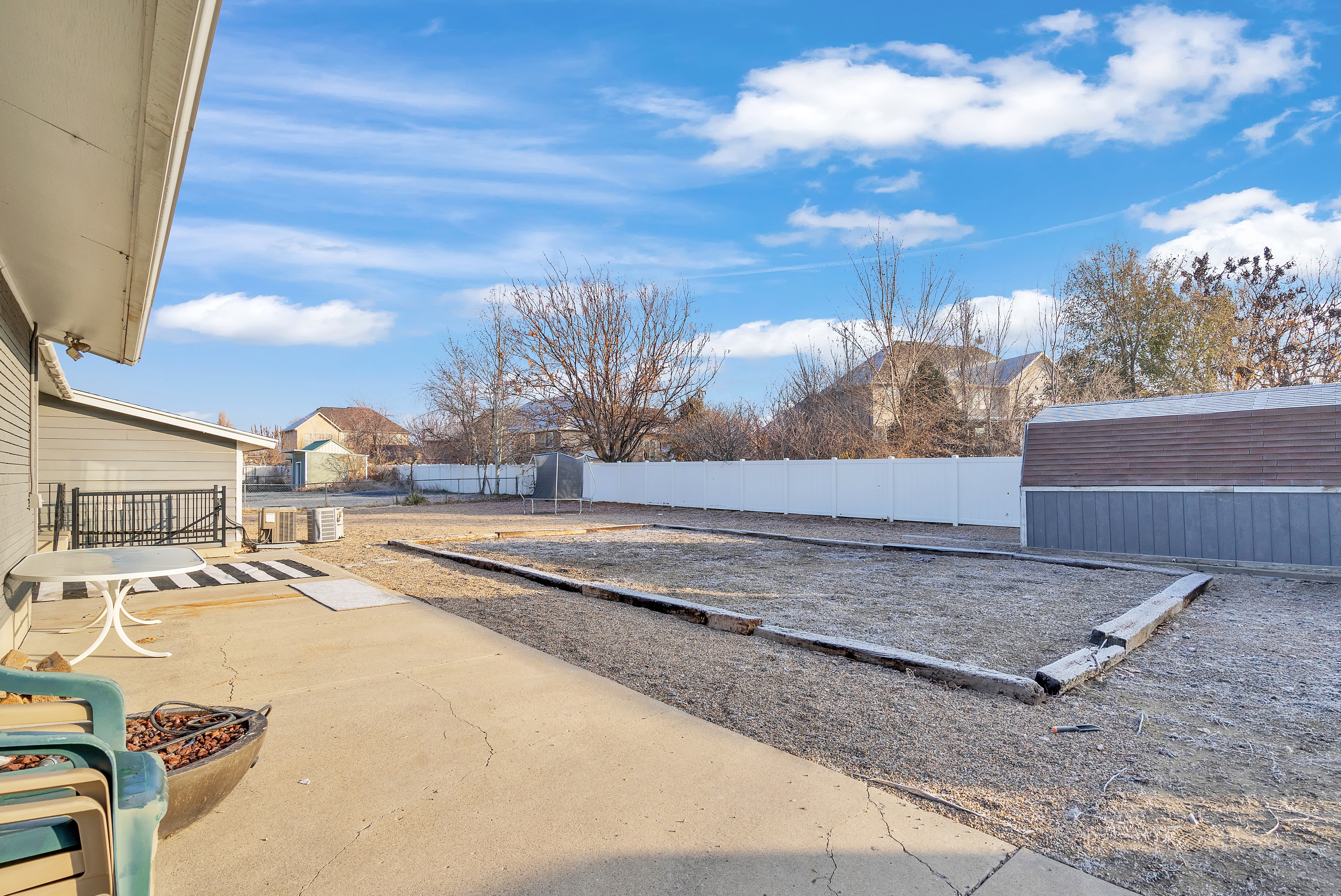 Expansive backyard featuring a concrete patio, white privacy fencing, and a detached storage shed with a brown roof and blue siding