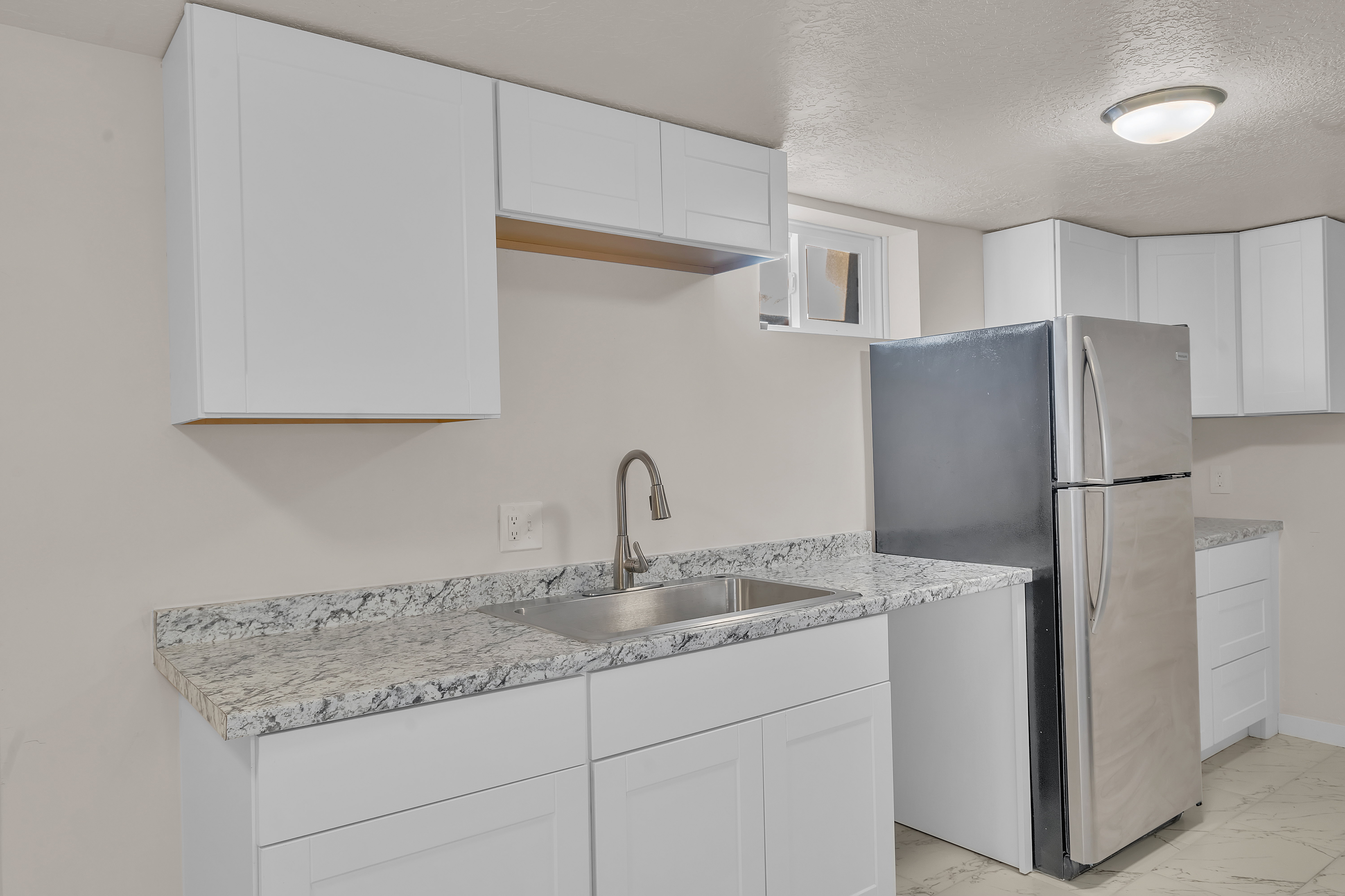 Kitchen featuring white shaker-style cabinetry, granite-patterned countertops, a stainless steel sink with a gooseneck faucet, and a stainless steel refrigerator
