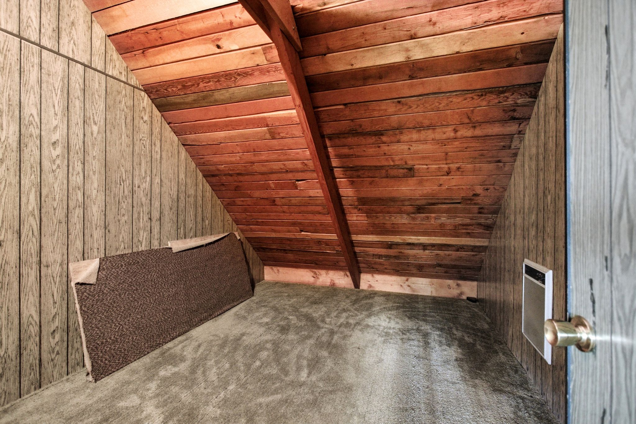 Angled room featuring wood-paneled walls and a sloped wood-plank ceiling with exposed beam