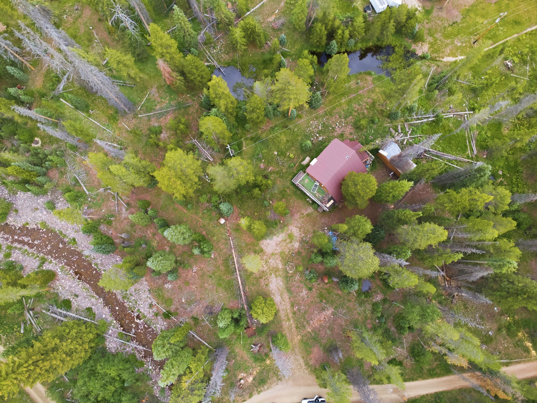 Aerial perspective showcasing a property surrounded by mature trees, featuring a main structure with a red roof, an additional outbuilding, and a visible body of water