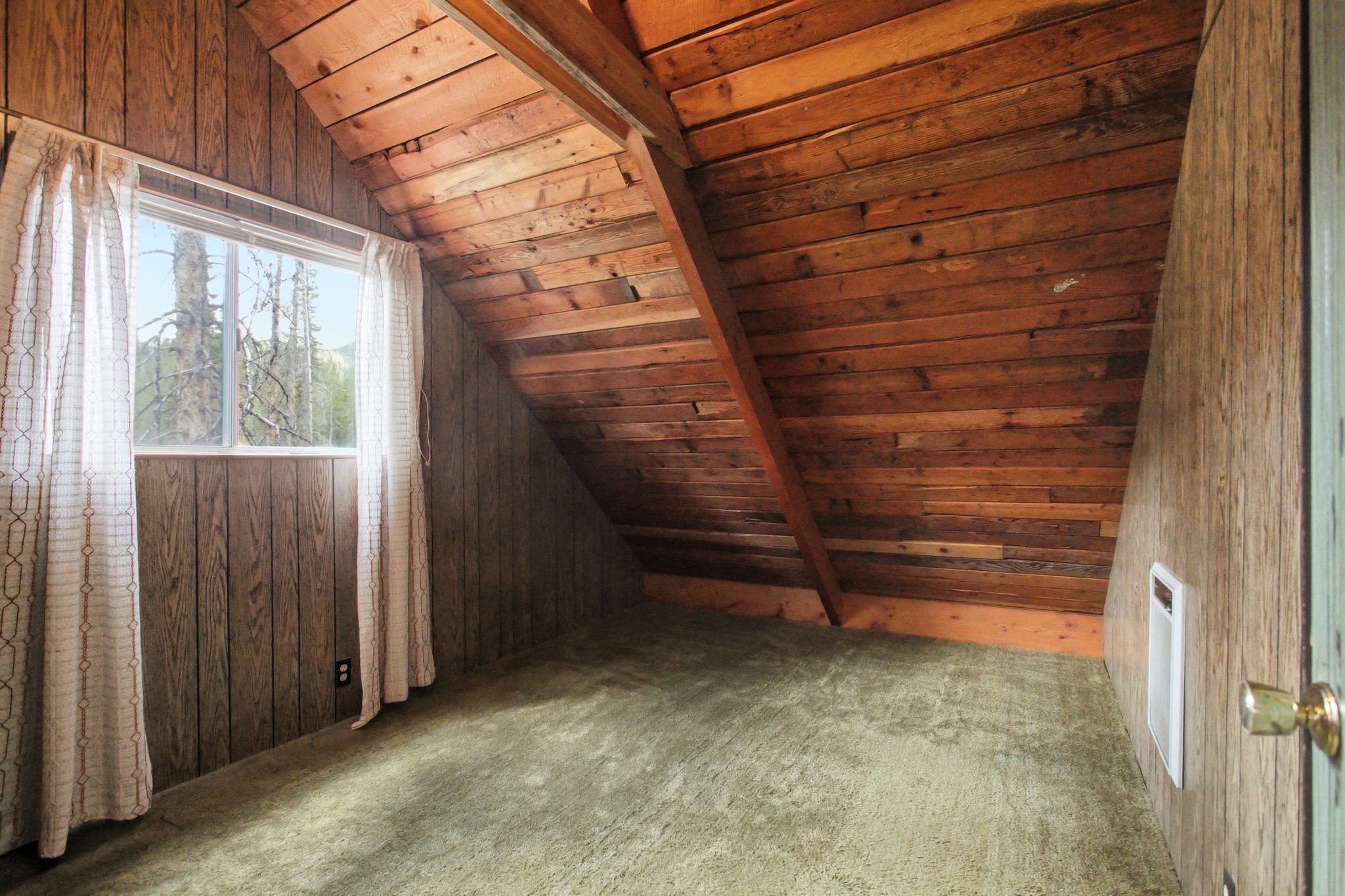 Windowed attic space featuring wood paneling, wood-planked sloped ceilings, and green-hued carpet flooring