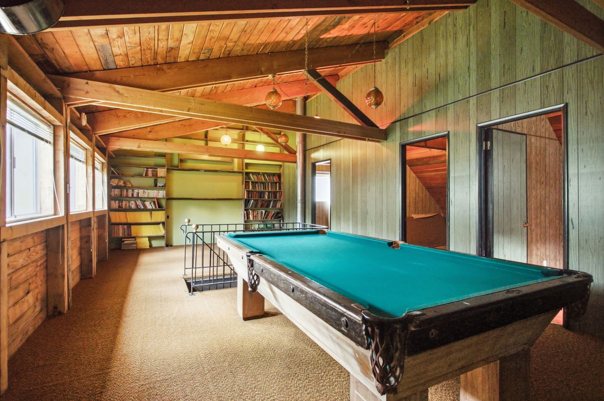 Recreation room featuring exposed wood beam ceiling, wood-paneled walls, built-in shelving, and multiple windows