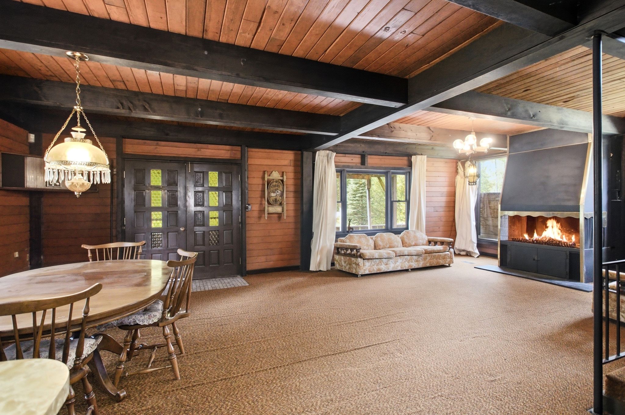 Expansive interior space featuring a floor-to-ceiling fireplace, exposed wood-beam ceiling, wood-paneled walls, and double entry doors with decorative glass inserts
