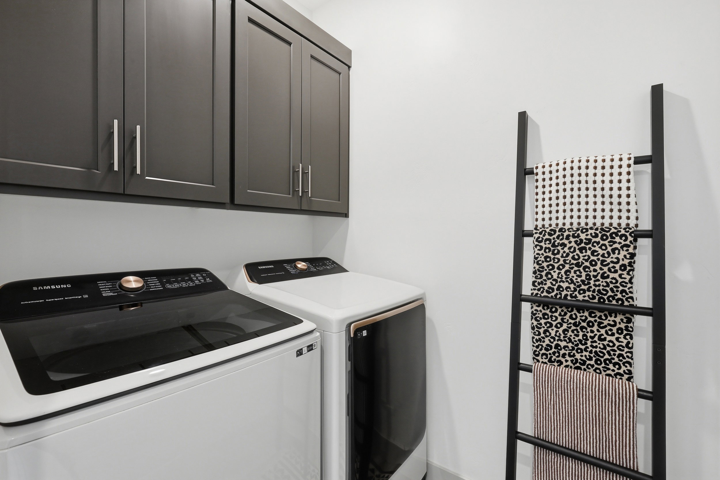 Laundry area featuring dark gray upper cabinetry with brushed nickel hardware, white walls, and a light gray baseboard