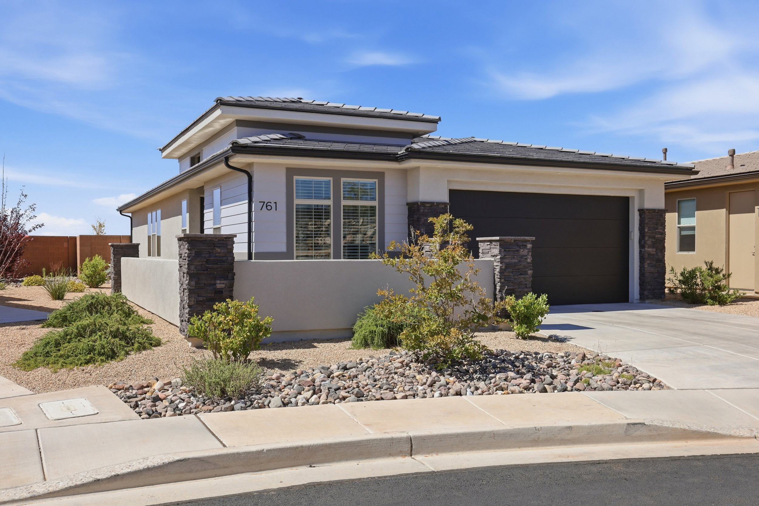 Contemporary architecture featuring a stone veneer facade, integrated two-car garage, and a low-maintenance xeriscaped front yard