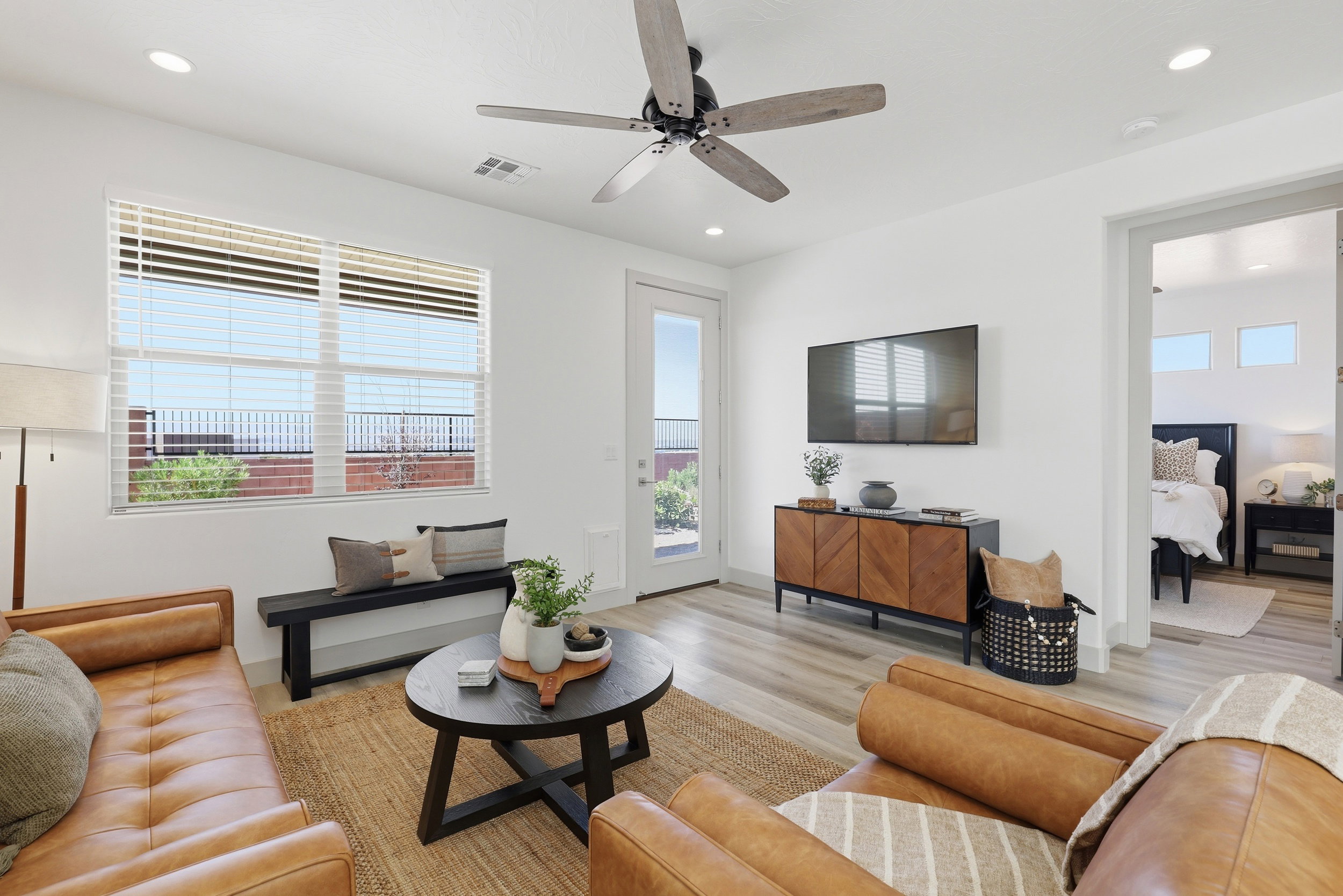 Spacious living area featuring light wood-finish flooring, a contemporary ceiling fan, recessed lighting, and a large window with horizontal blinds