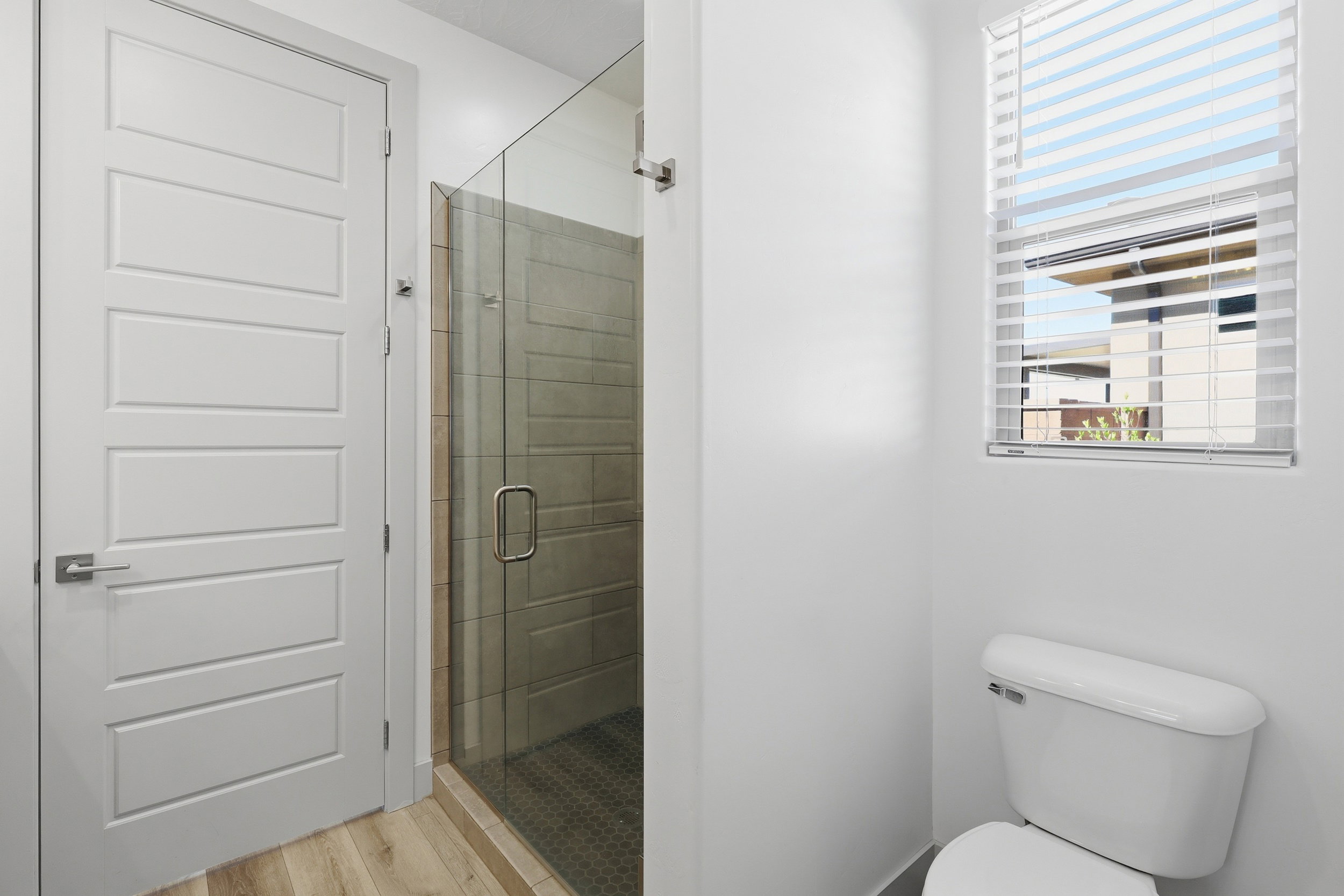Glass-enclosed shower with horizontal tile surround and dark hex-tile flooring