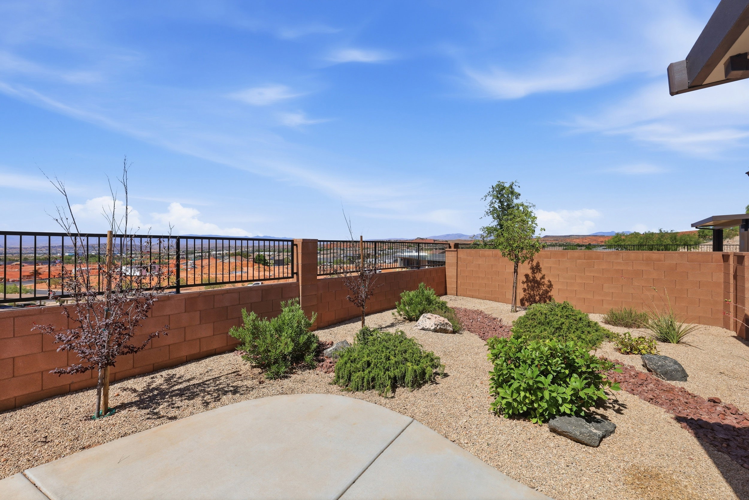 Expansive xeriscaped backyard featuring a concrete patio, a block retaining wall, and a black metal fence