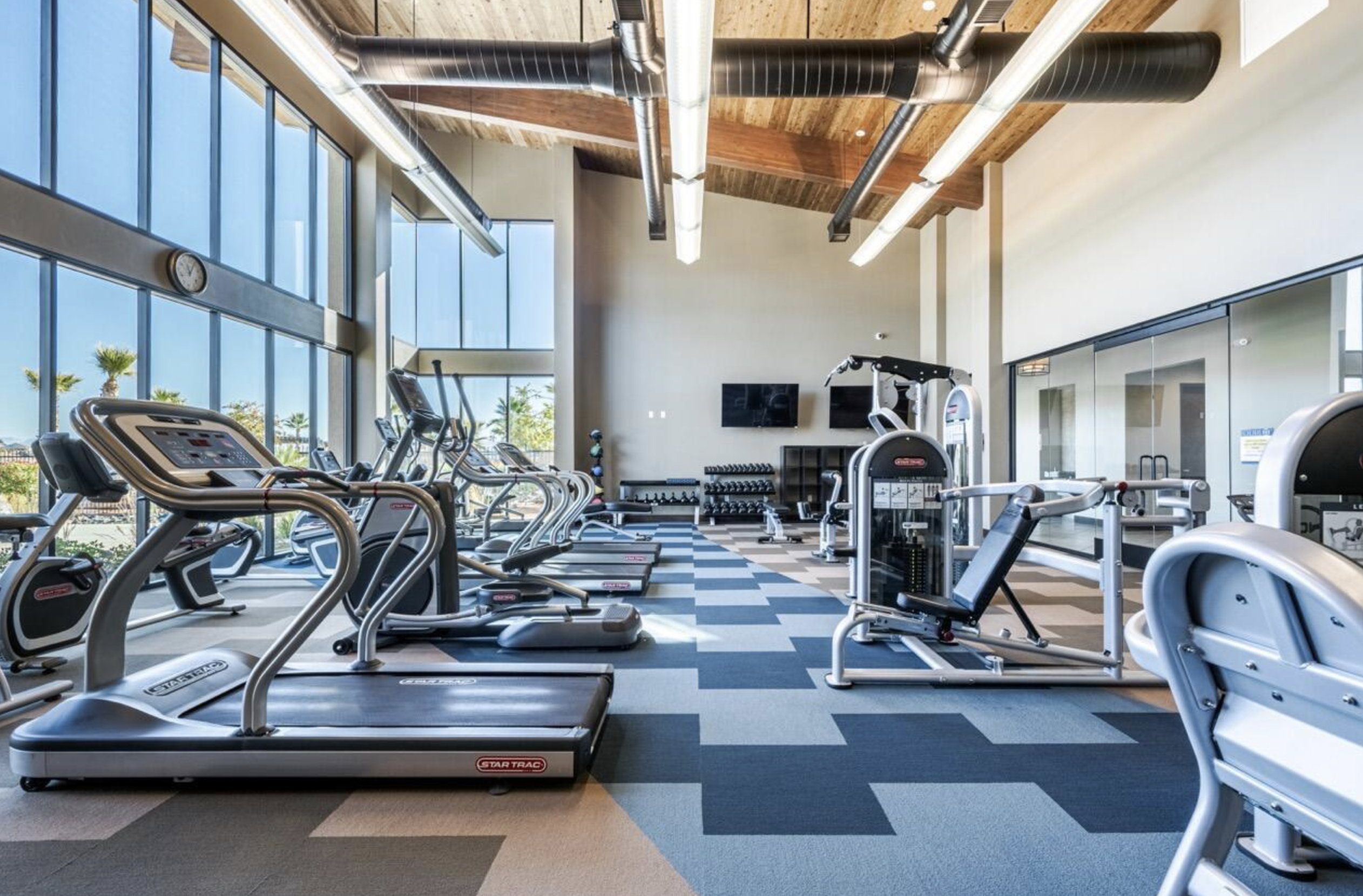 Fitness center featuring high ceilings, extensive window walls, patterned carpet flooring, exposed ductwork, and various exercise equipment