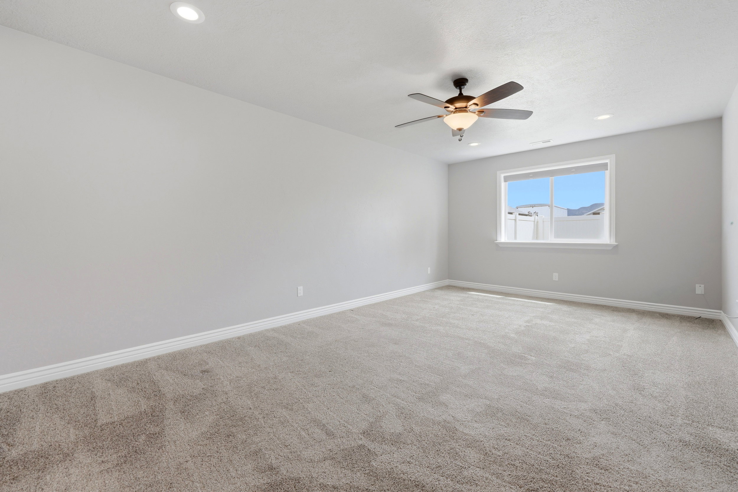 Spacious room featuring neutral wall paint, light gray carpeting, a multi-blade ceiling fan with integrated lighting, recessed lighting, and a large window with white trim